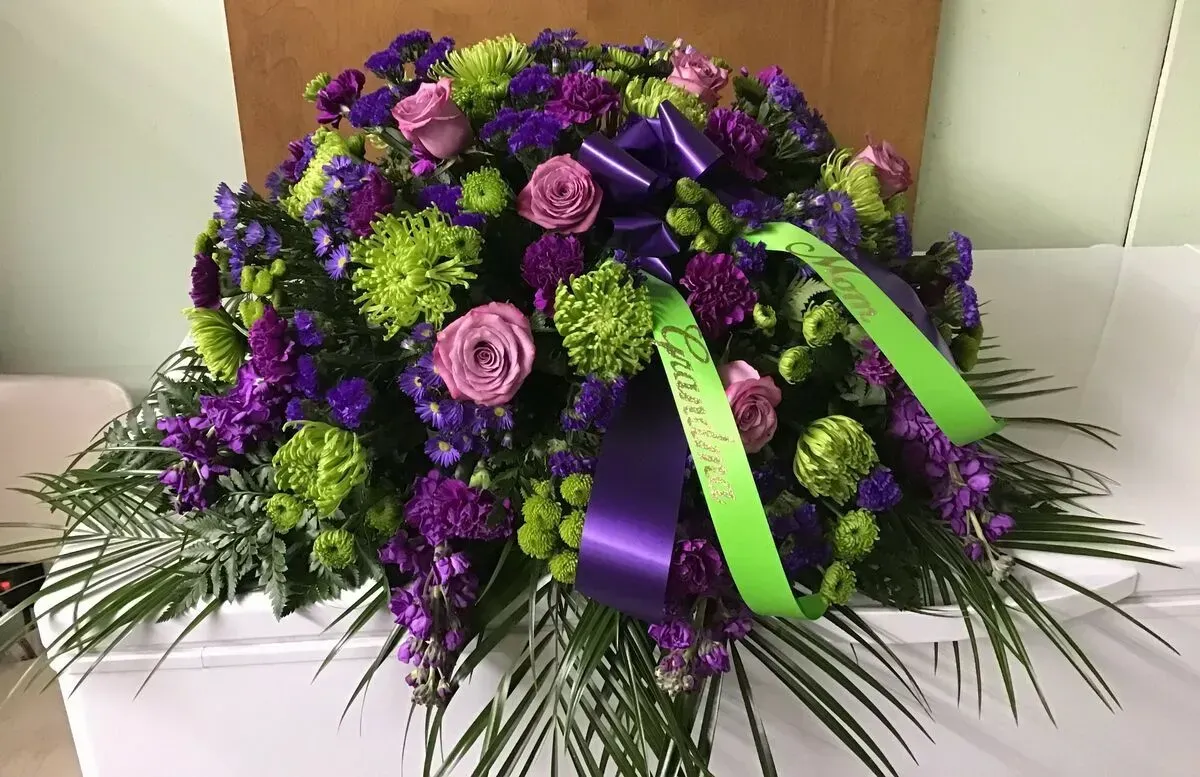 Purple and green floral casket spray with ribbon.