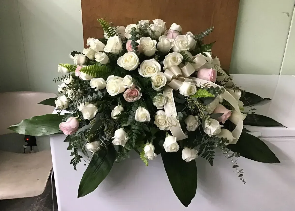 White and pink rose floral arrangement with greenery and a white ribbon.