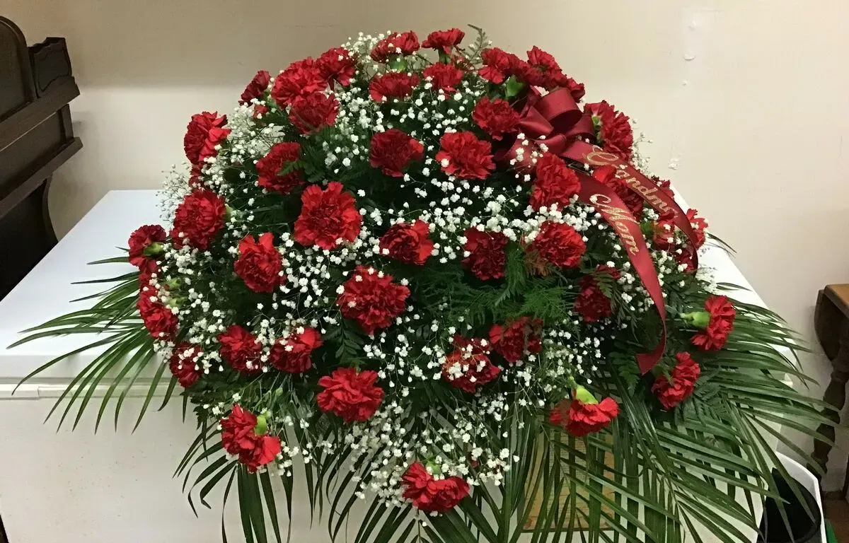 Red carnation floral arrangement on a white surface, accented with baby's breath, and a red bow.