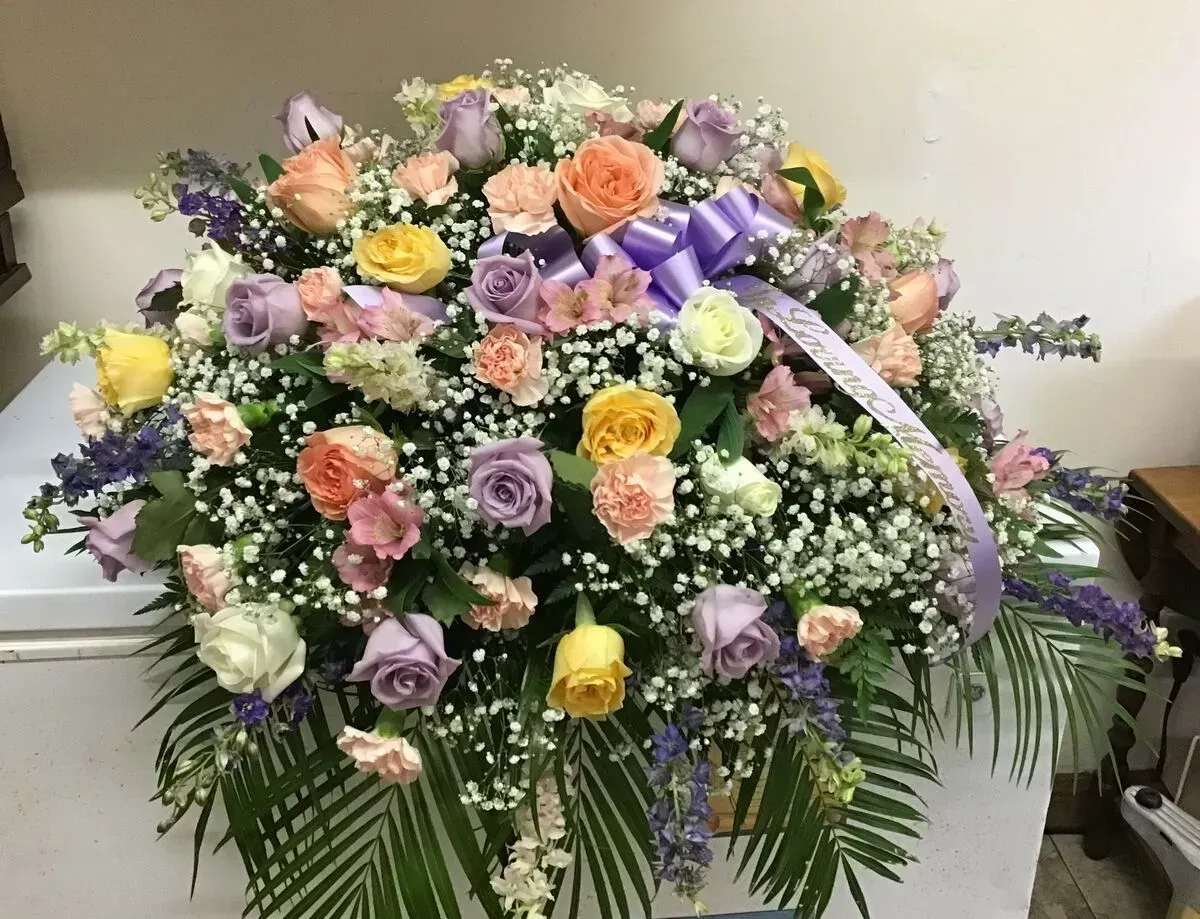 Floral arrangement in pastel colors with a purple bow on a white surface.