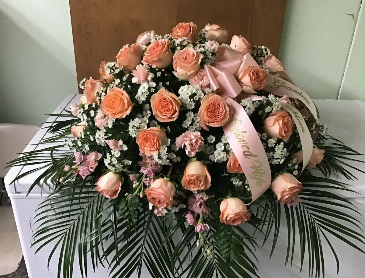 Floral arrangement of peach roses, carnations, baby's breath, and greenery, with a pink ribbon.