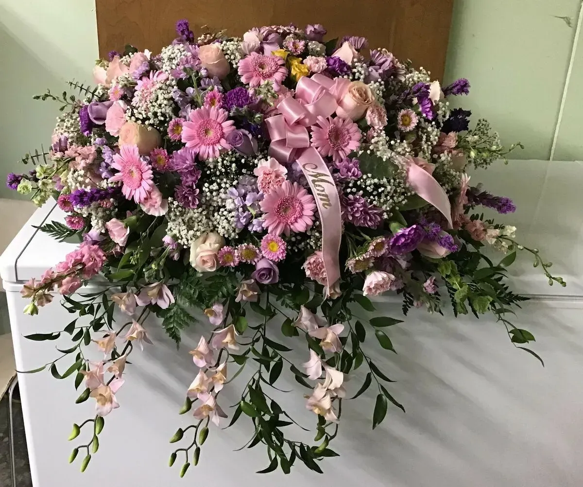 Floral arrangement on a white surface, mostly pink and purple flowers with a Mom ribbon.