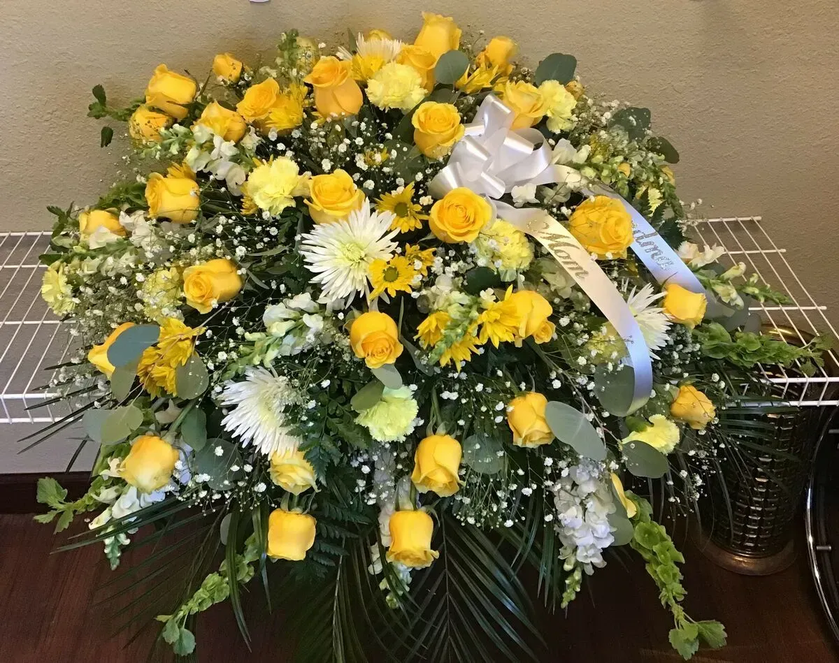 Floral arrangement of yellow roses and white flowers with a ribbon.