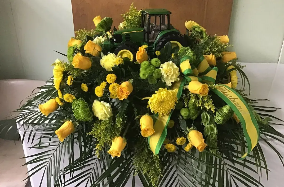 Floral arrangement with yellow roses, green foliage, and a toy tractor.