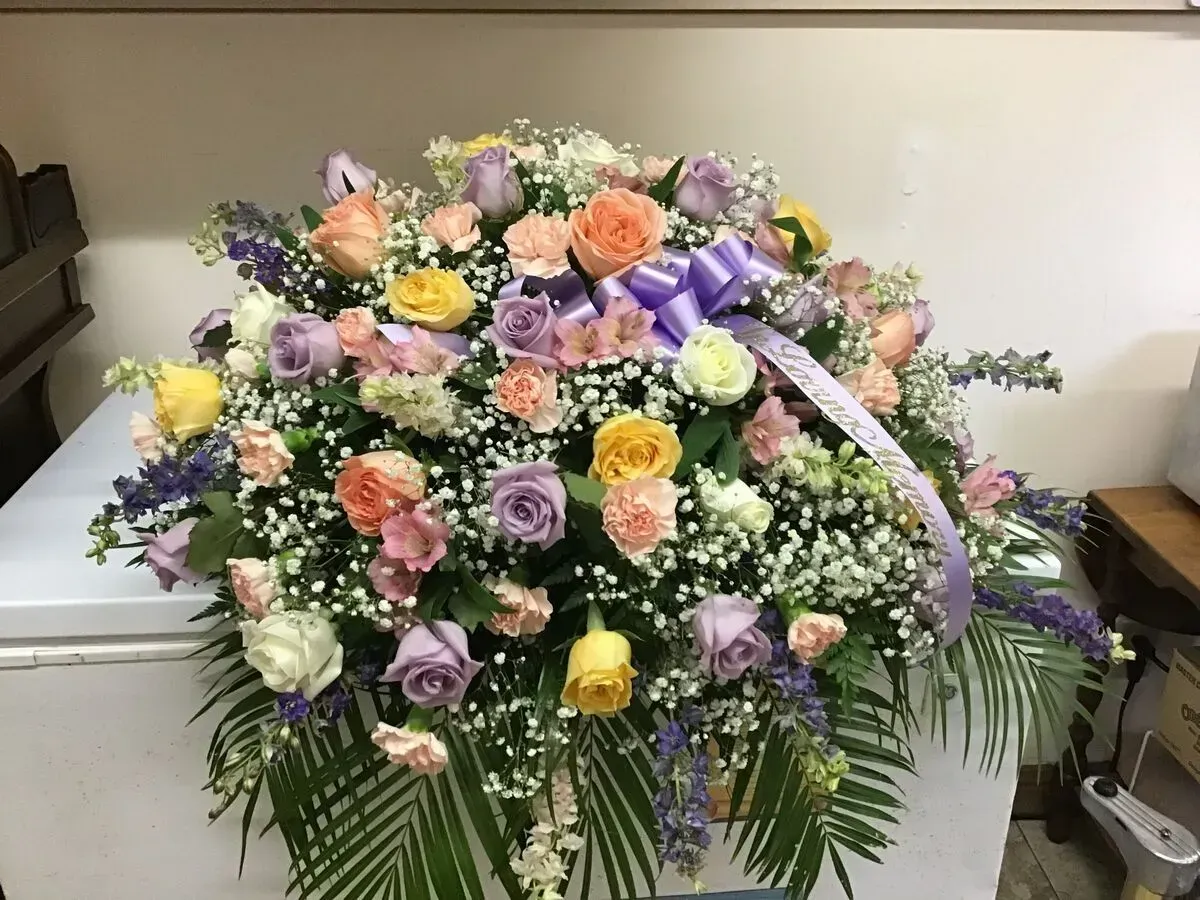Floral arrangement of pastel roses, carnations, and greenery, with a purple bow.