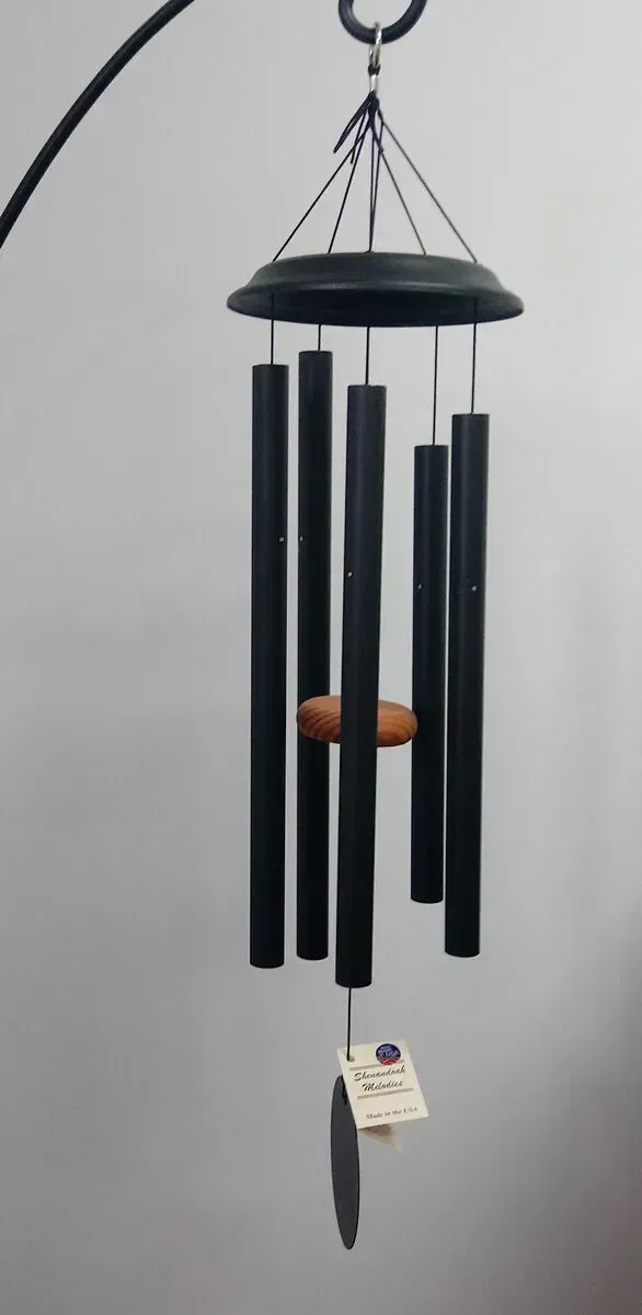 Black wind chimes hanging against a light gray wall.