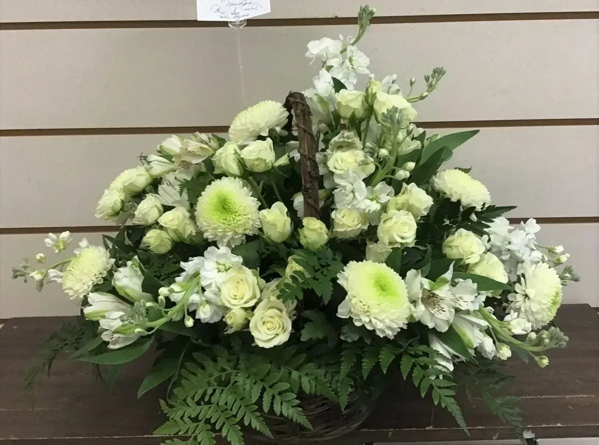 White floral arrangement in a basket, with chrysanthemums, roses, and greenery.