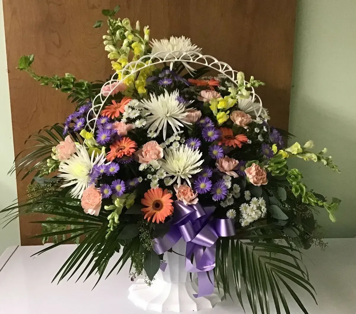 Basket of colorful flowers, including white, orange, and purple, with a purple ribbon.
