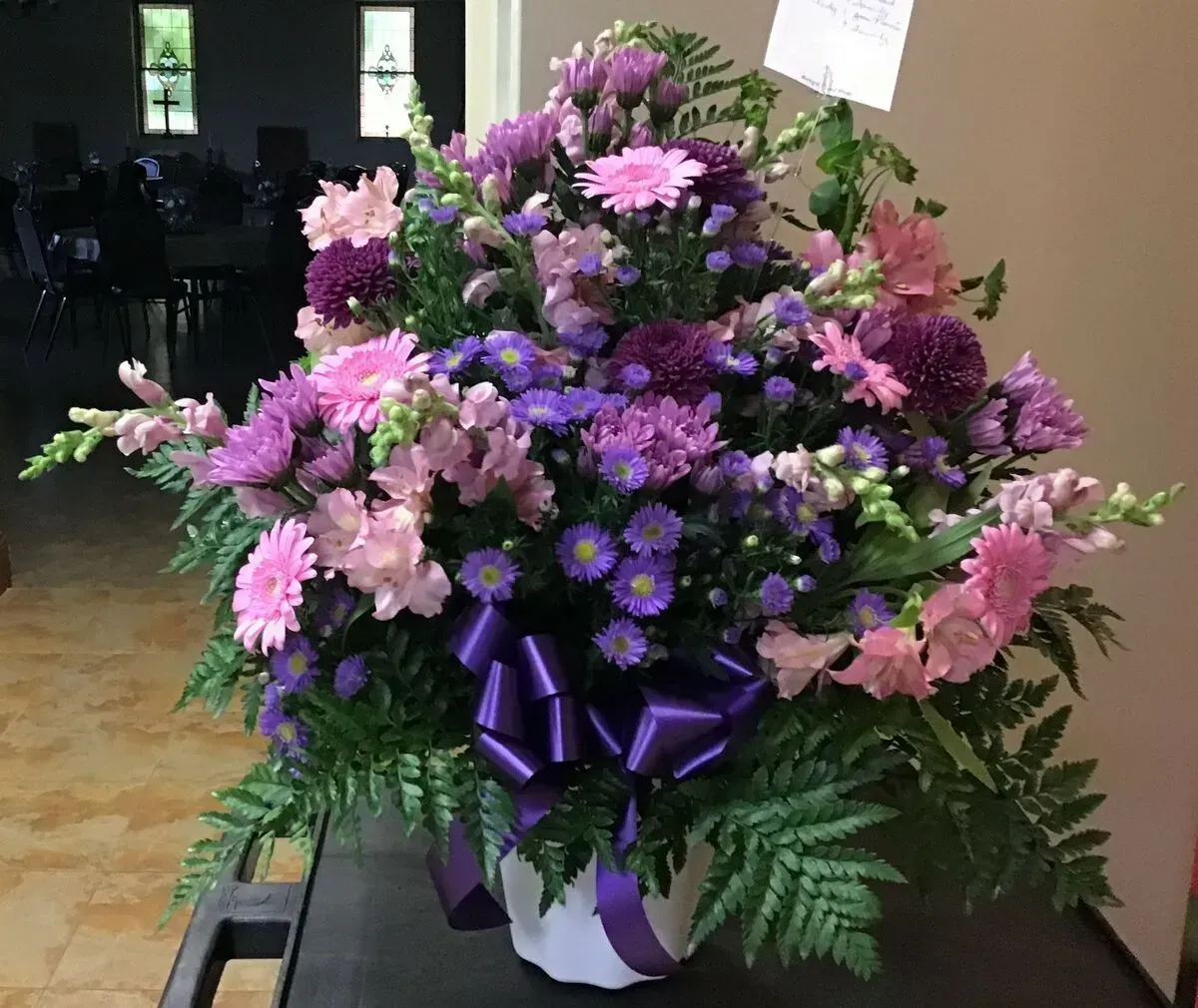 Purple and pink floral arrangement in a white pot with a purple bow.