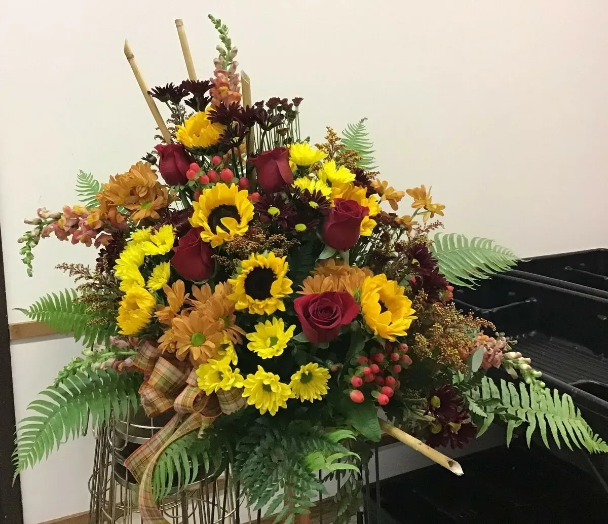 Floral arrangement with sunflowers, roses, and greenery. Yellow, red, and brown tones.