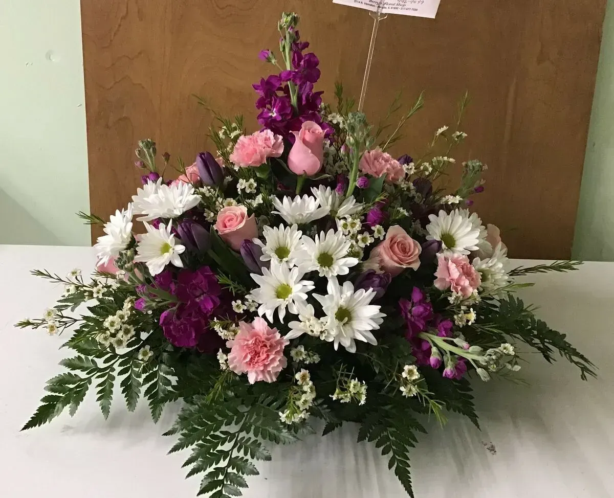 Floral arrangement with pink and white flowers, purple accents, and greenery on a table.