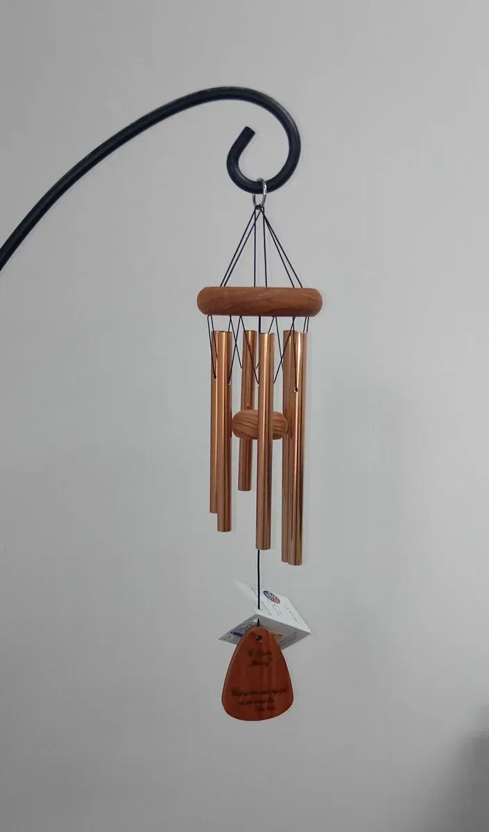 Wind chimes with bronze tubes and a wooden top and striker, hanging from a black hook.