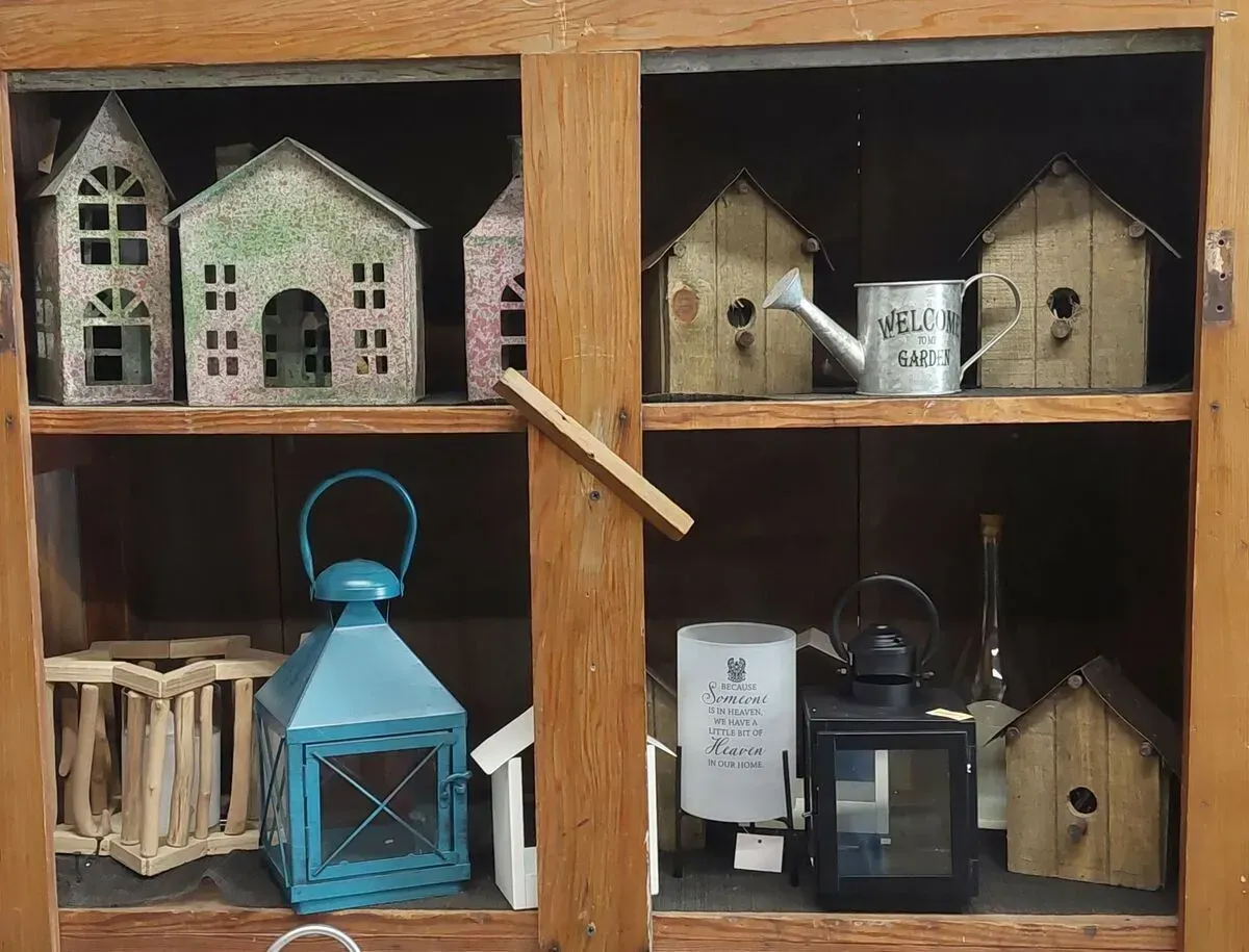Wooden cabinet with decorative houses, lanterns, and a watering can on shelves.