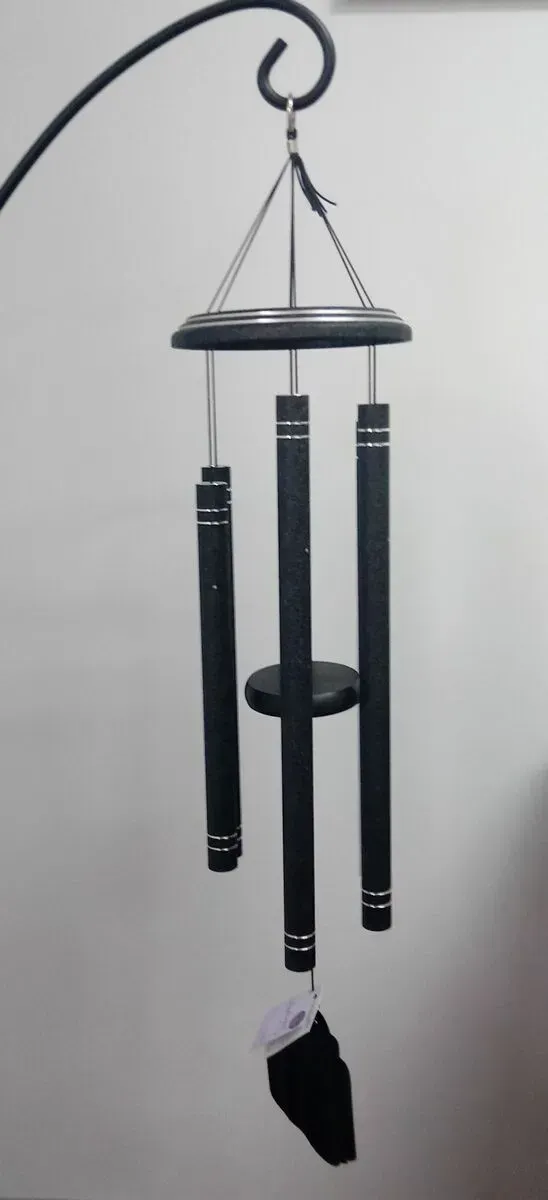 Black wind chimes hanging from a black hook with a white wall in the background.