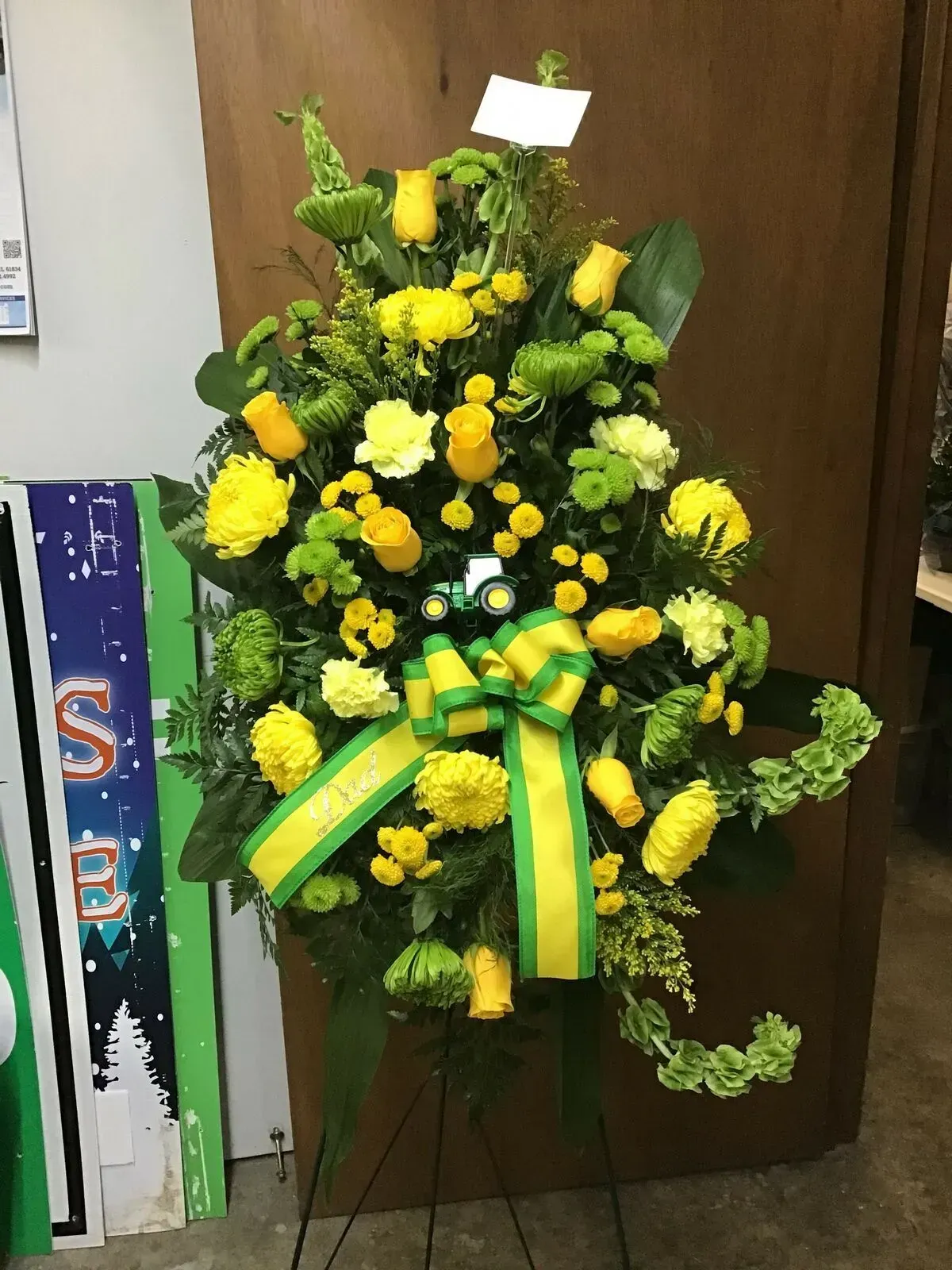Floral arrangement of yellow and green flowers with a matching bow on a black stand.