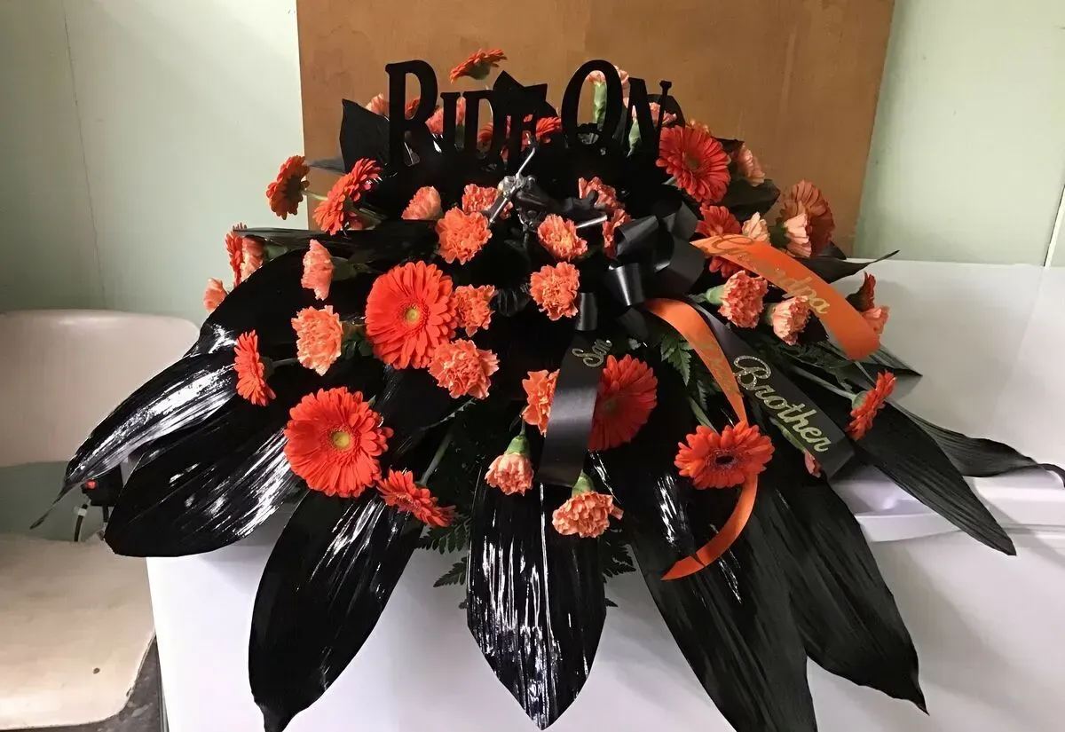 Funeral arrangement: Orange flowers with black accents and a ribbon that says Brother.