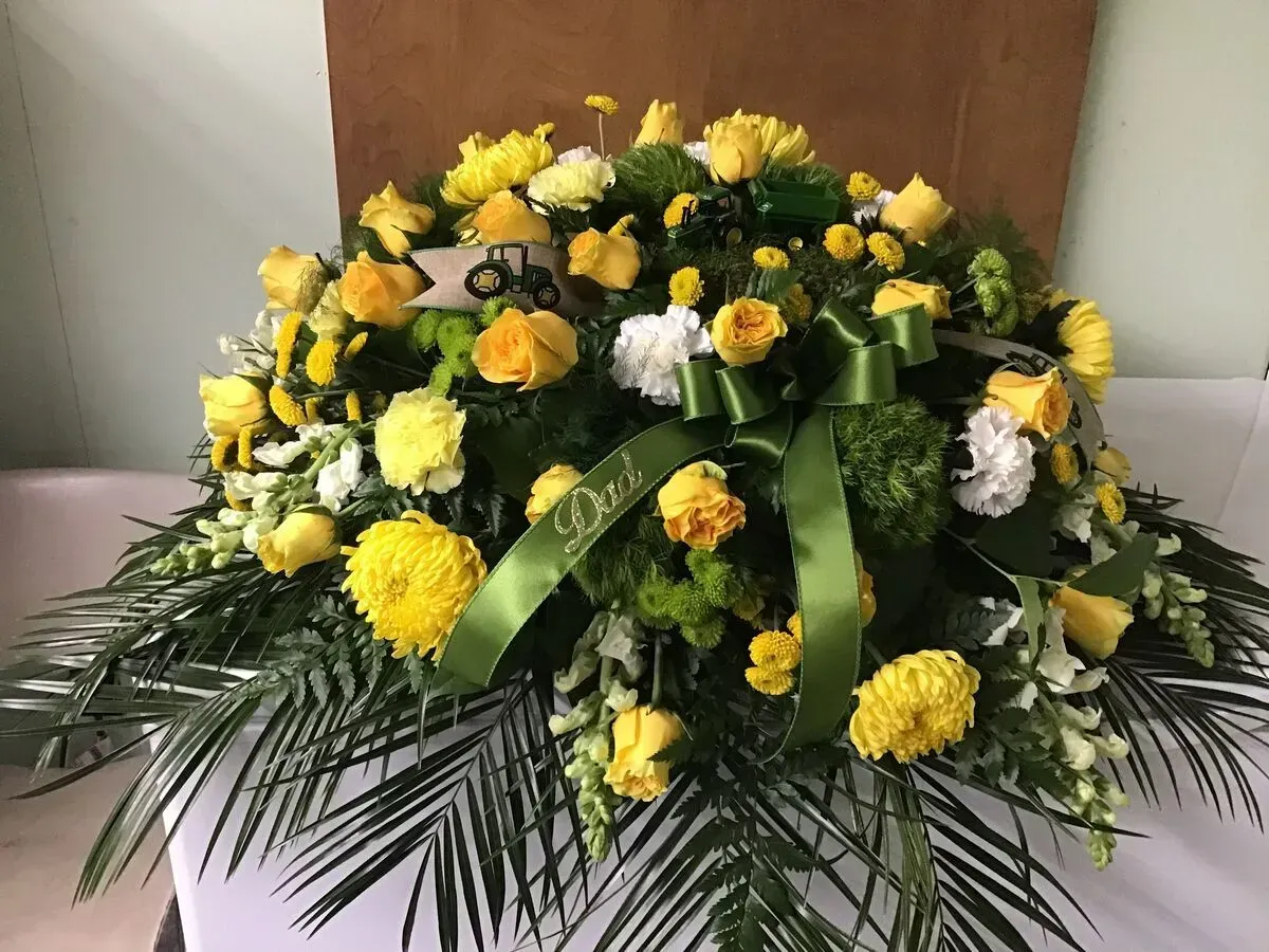 Yellow floral arrangement with green foliage and a green ribbon.