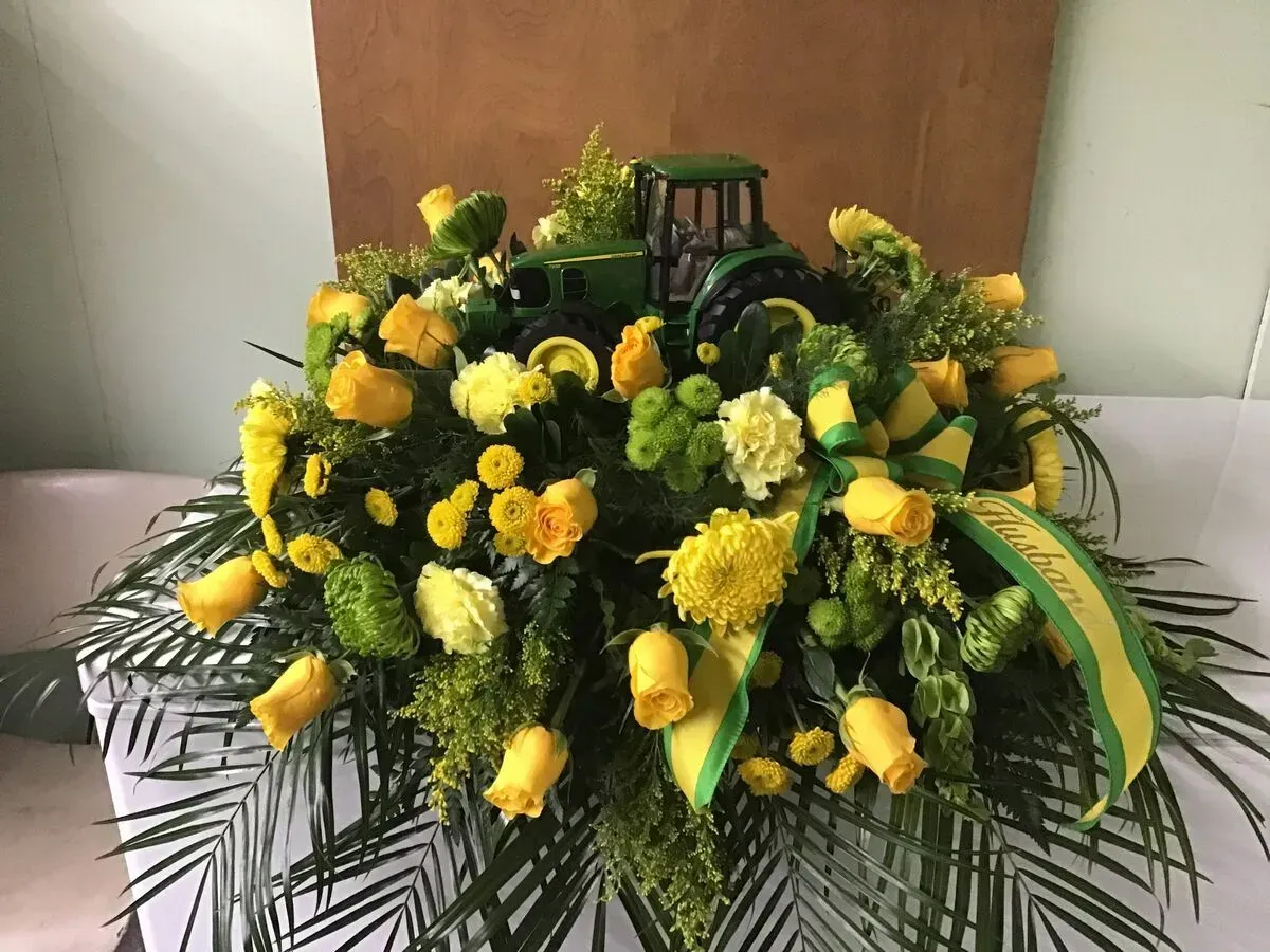 Floral arrangement with John Deere tractor, yellow roses, and green accents.