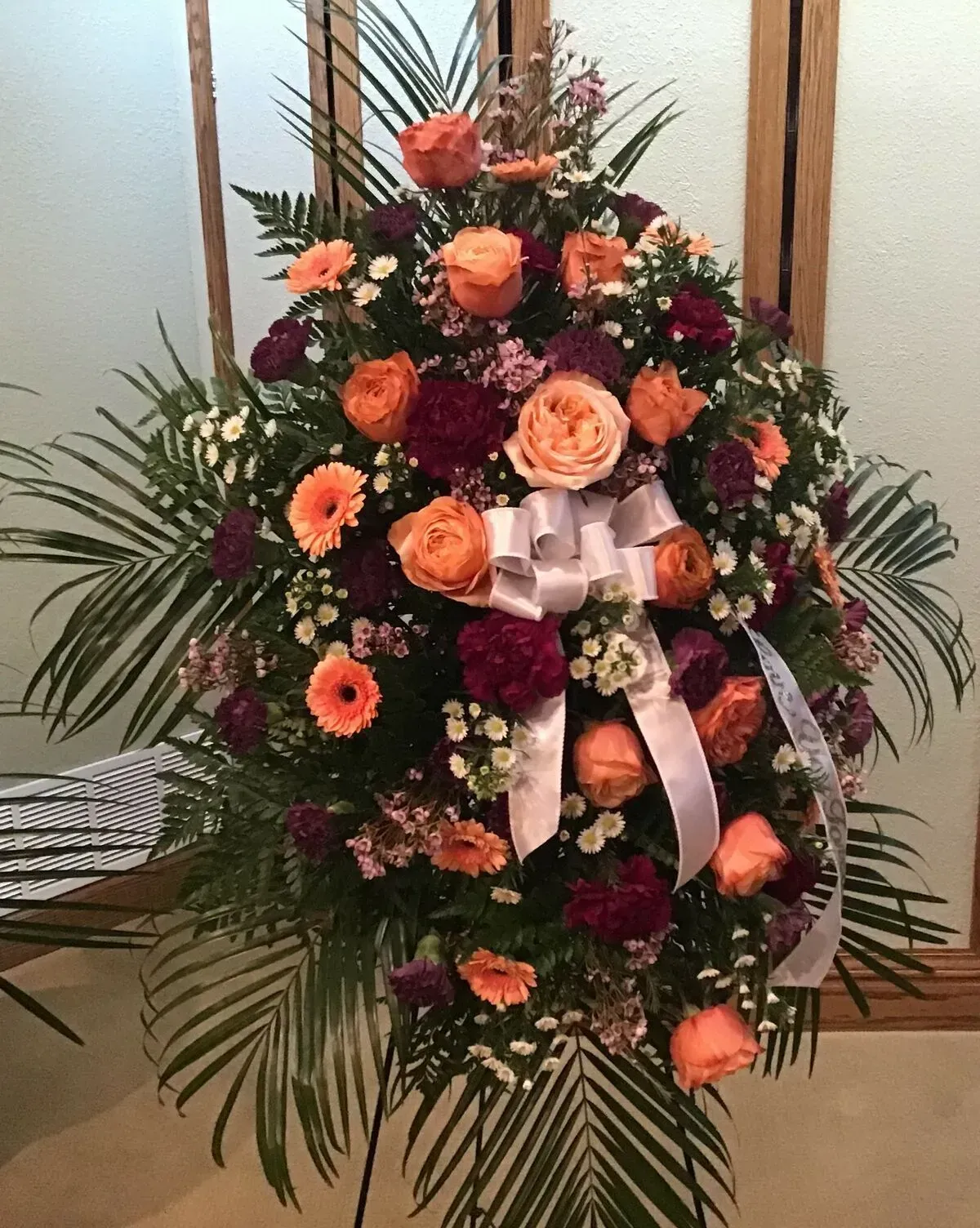 Floral arrangement of orange and burgundy flowers with a white ribbon.