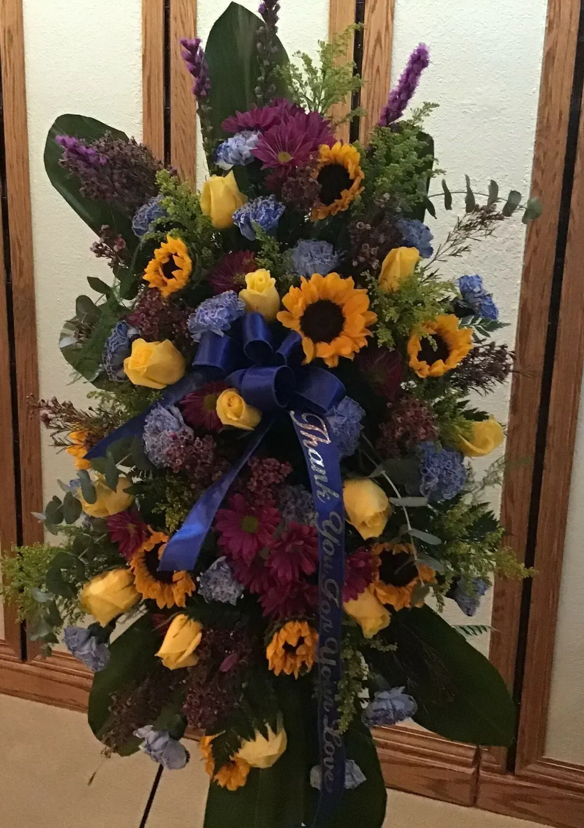 Floral arrangement with sunflowers, yellow roses, and blue bow.