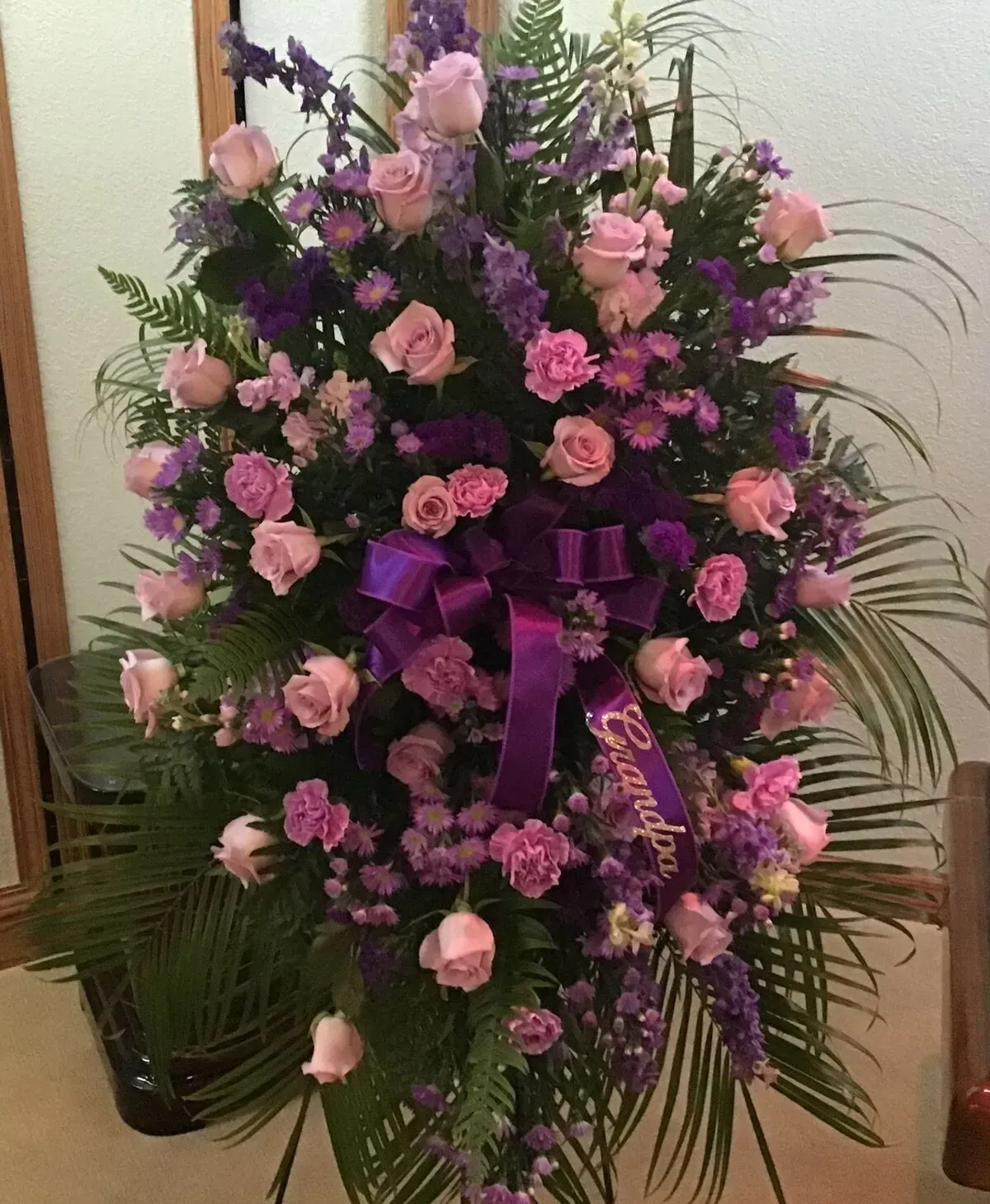 Purple and pink floral arrangement on a stand, with a bow.