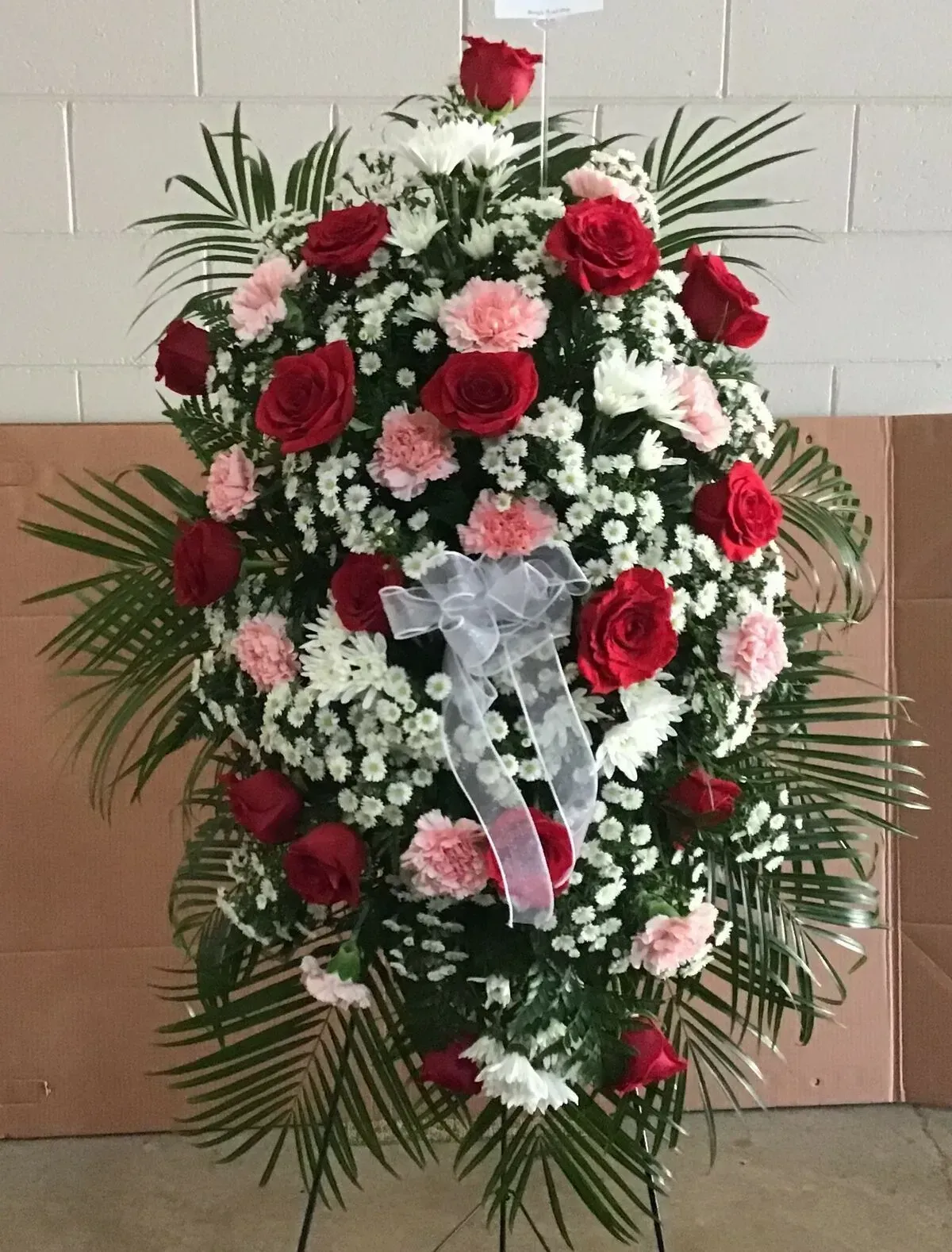 A flower arrangement of red roses, pink carnations, white flowers, and greenery on a stand.