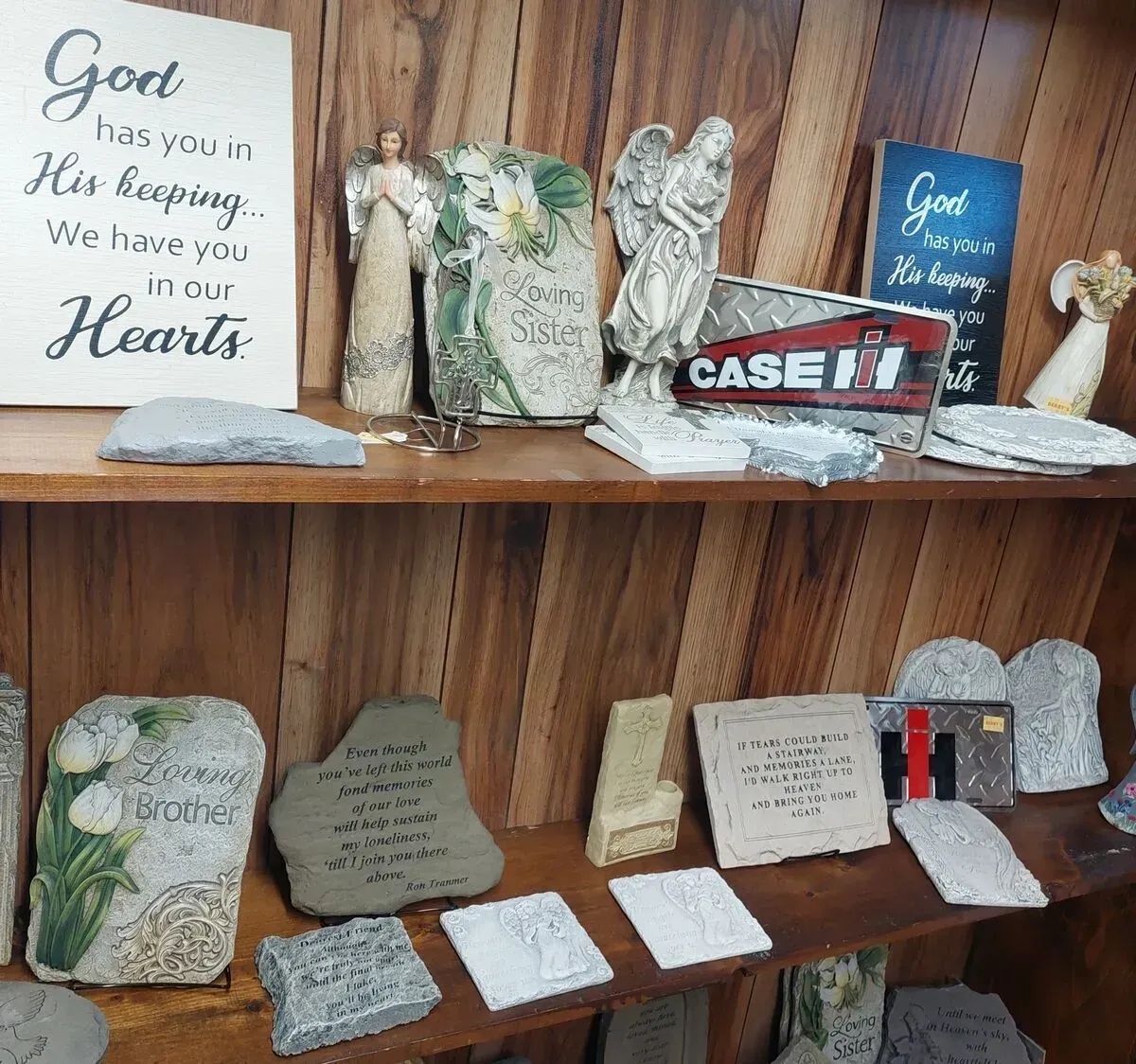 Wooden shelves displaying angel figurines, stone memorials, and decorative signs with religious quotes.