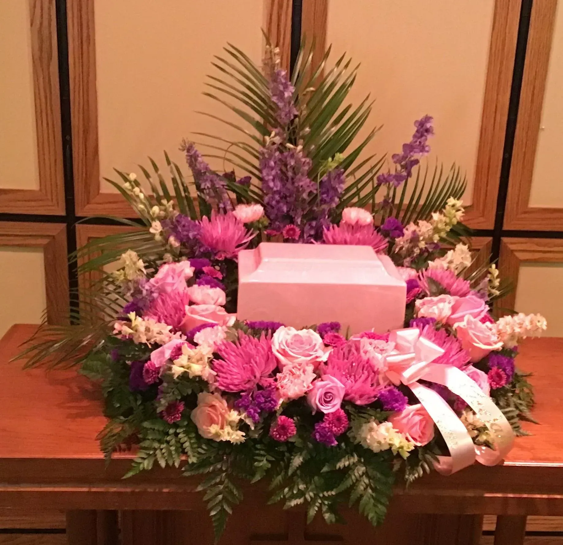 Pink urn surrounded by pink and purple flowers with a bow.