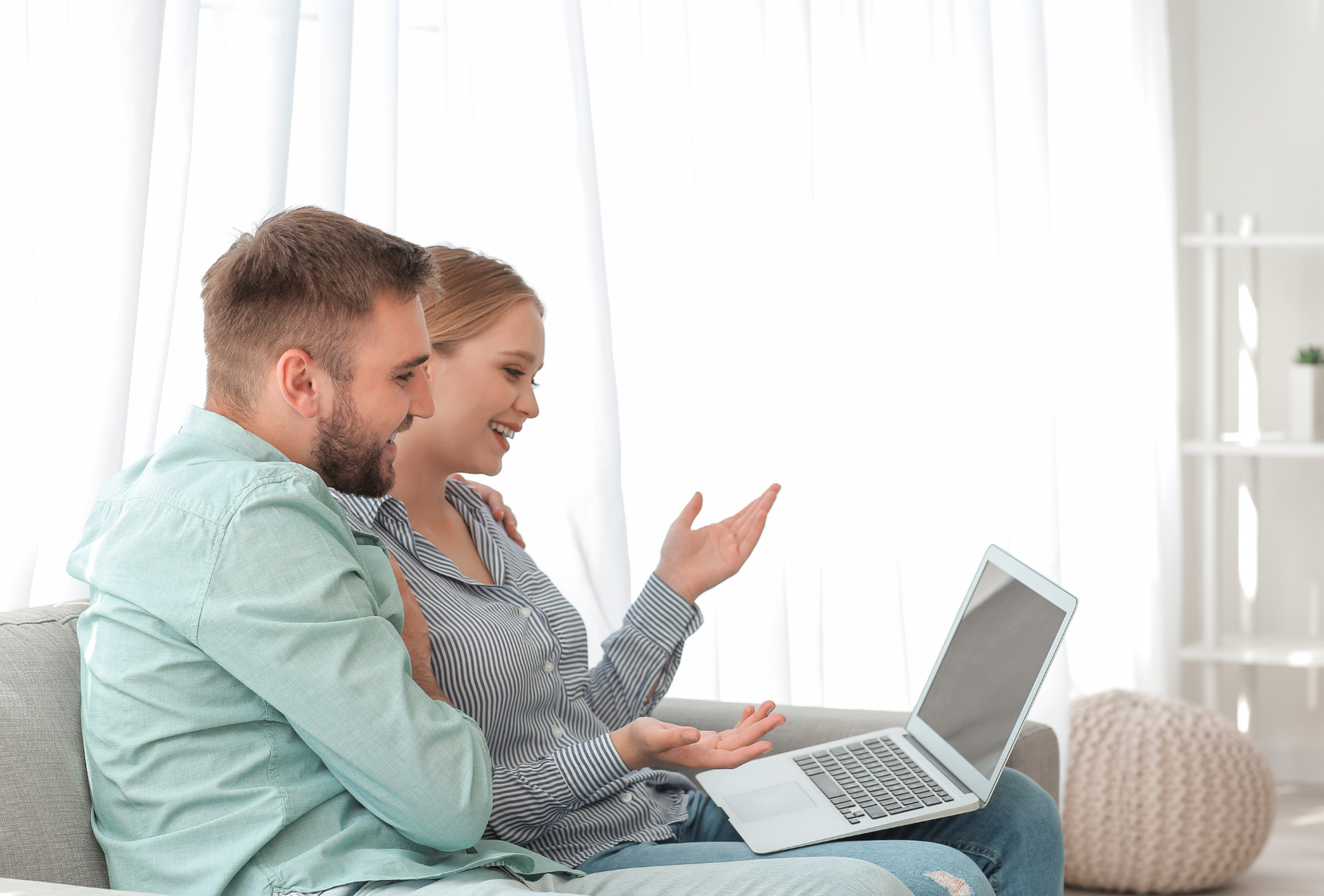 A man and a woman are sitting on a couch looking at a laptop.