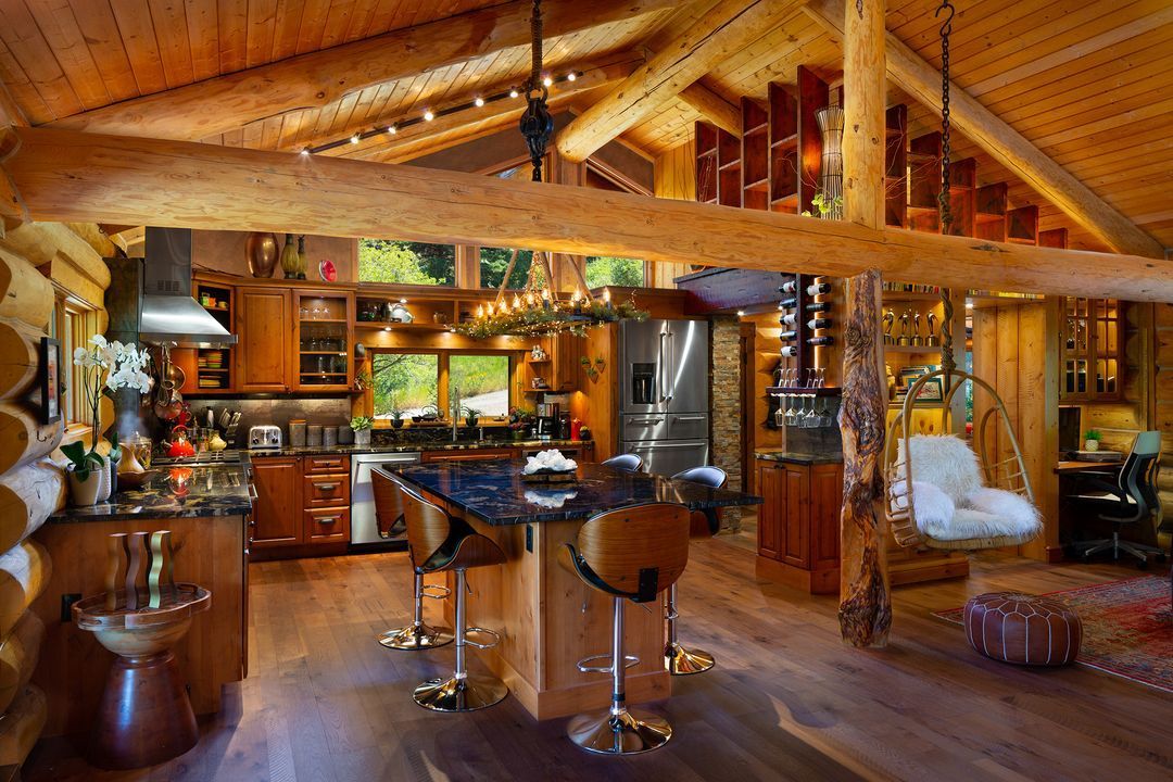 Rustic log cabin kitchen with wood beams, island with stools, and hanging chair.