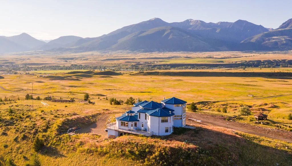 White house with blue roofs atop a hill, overlooking a valley and mountains.