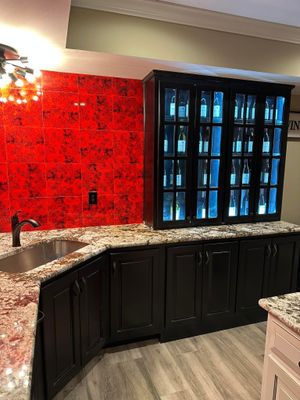 A bar area with black cabinetry, granite countertops, a metal sink, and a striking red brick wall backdrop.