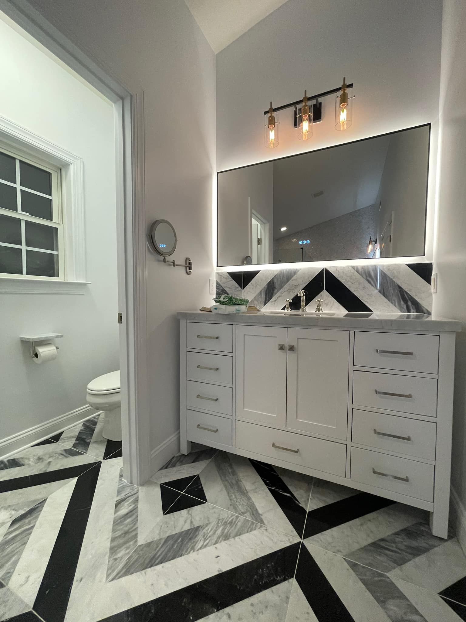 Modern bathroom with a white vanity, a backlit mirror, and black-and-white chevron-patterned marble floor and backsplash.