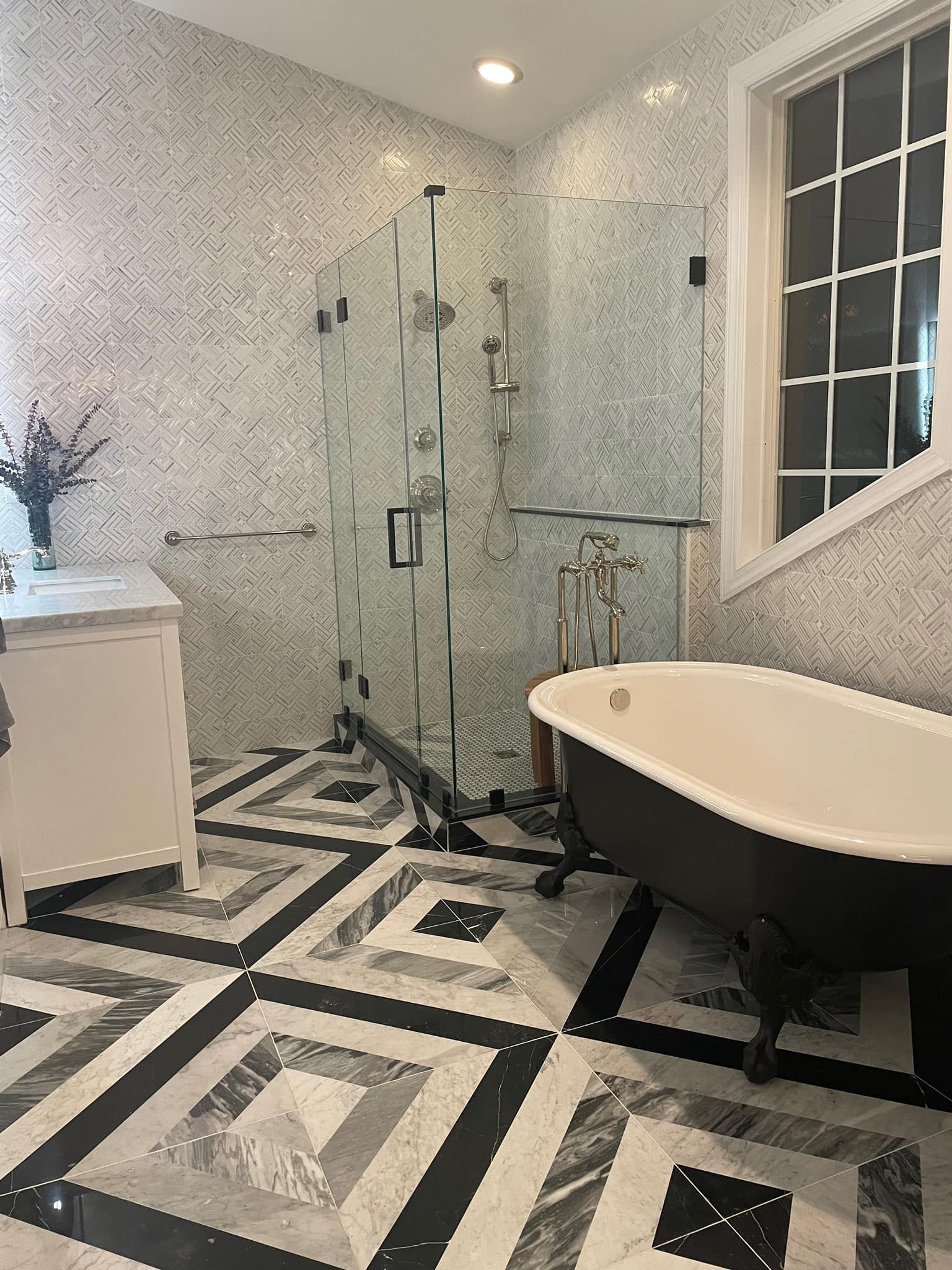 A luxurious bathroom featuring a black clawfoot tub, a glass-enclosed shower, and patterned marble tile floors and walls.