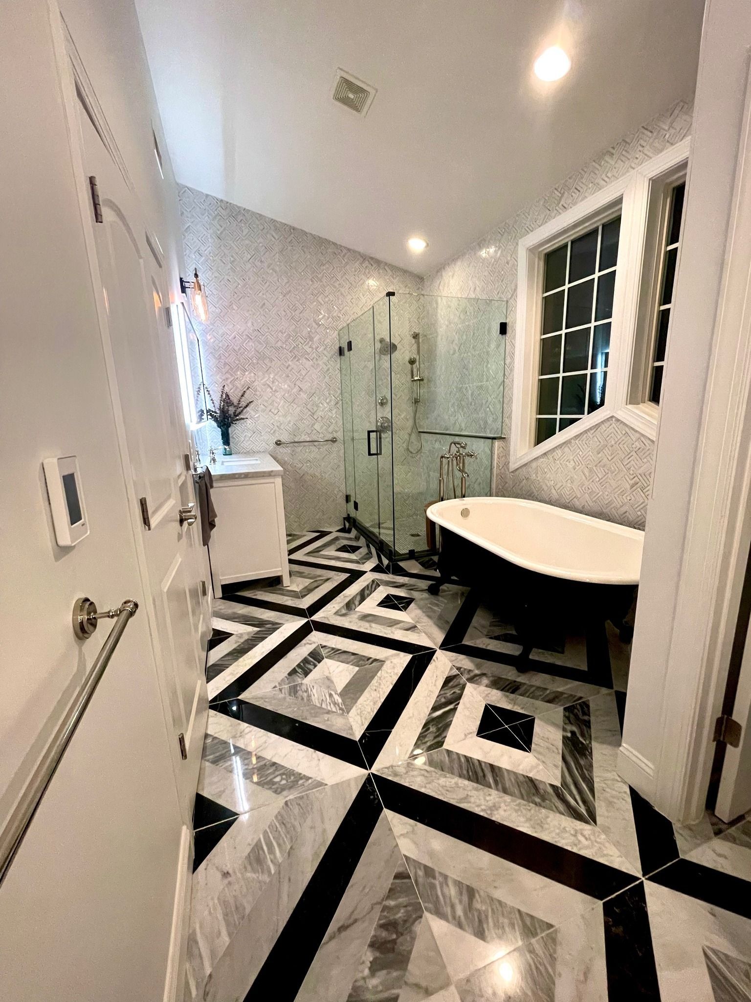 A modern bathroom featuring a white freestanding tub, a glass-enclosed shower, and striking geometric black-and-white tile.