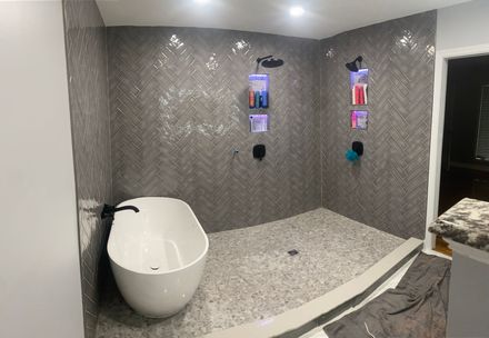 Modern bathroom with a freestanding white tub next to a walk-in shower featuring grey herringbone tiles and pebble floors.