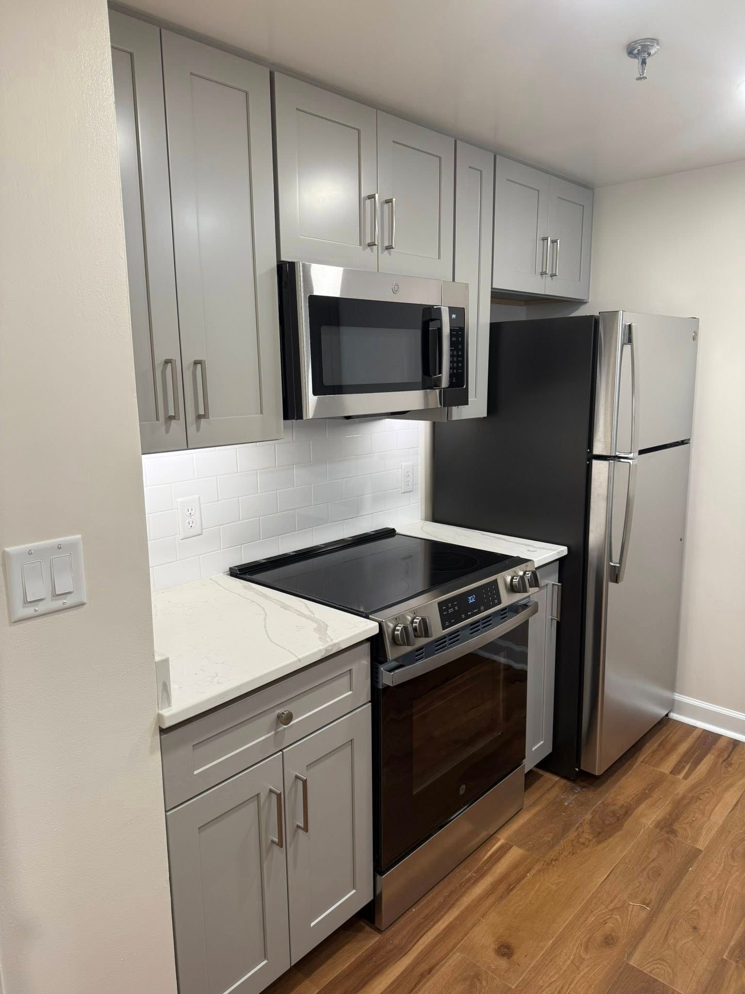 A modern galley kitchen featuring light gray cabinets, stainless steel appliances, a black stove, and light wood flooring.