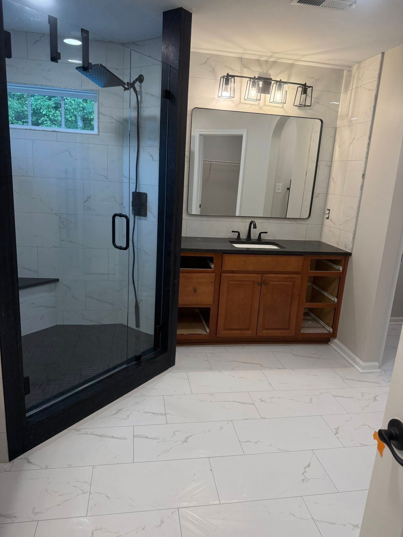 A modern bathroom with a glass-enclosed shower, white marble-style tiled floors, and a wooden vanity cabinet.