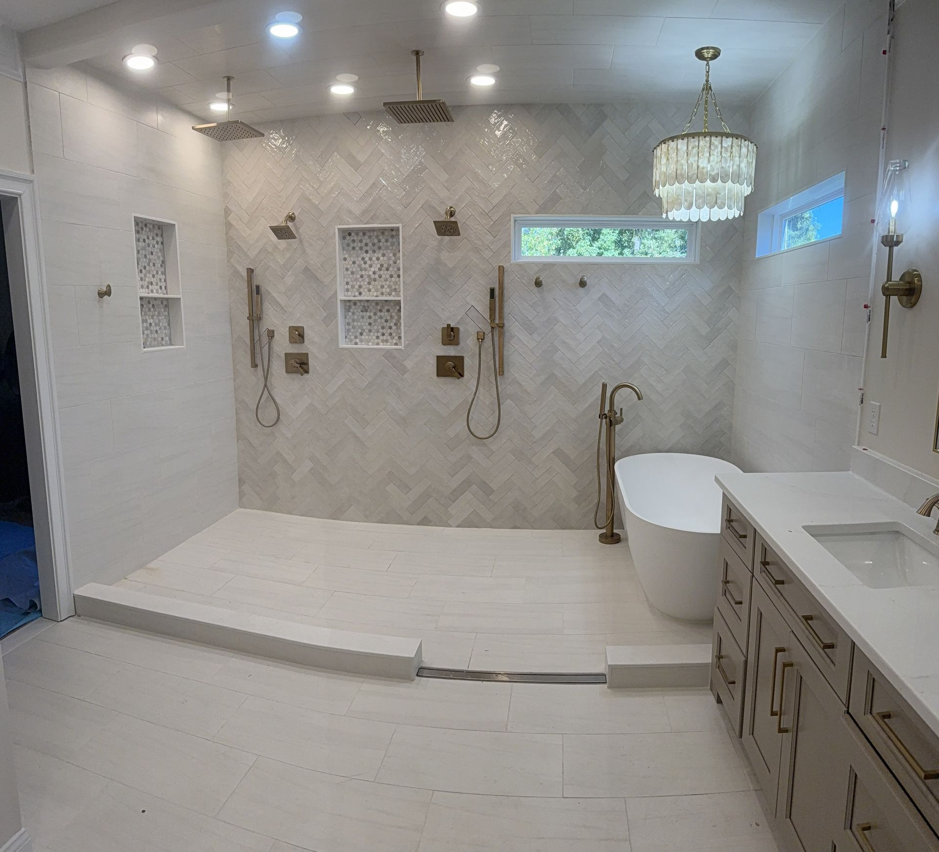 A luxurious bathroom with a walk-in shower, herringbone wall tile, a freestanding bathtub, and a double vanity.