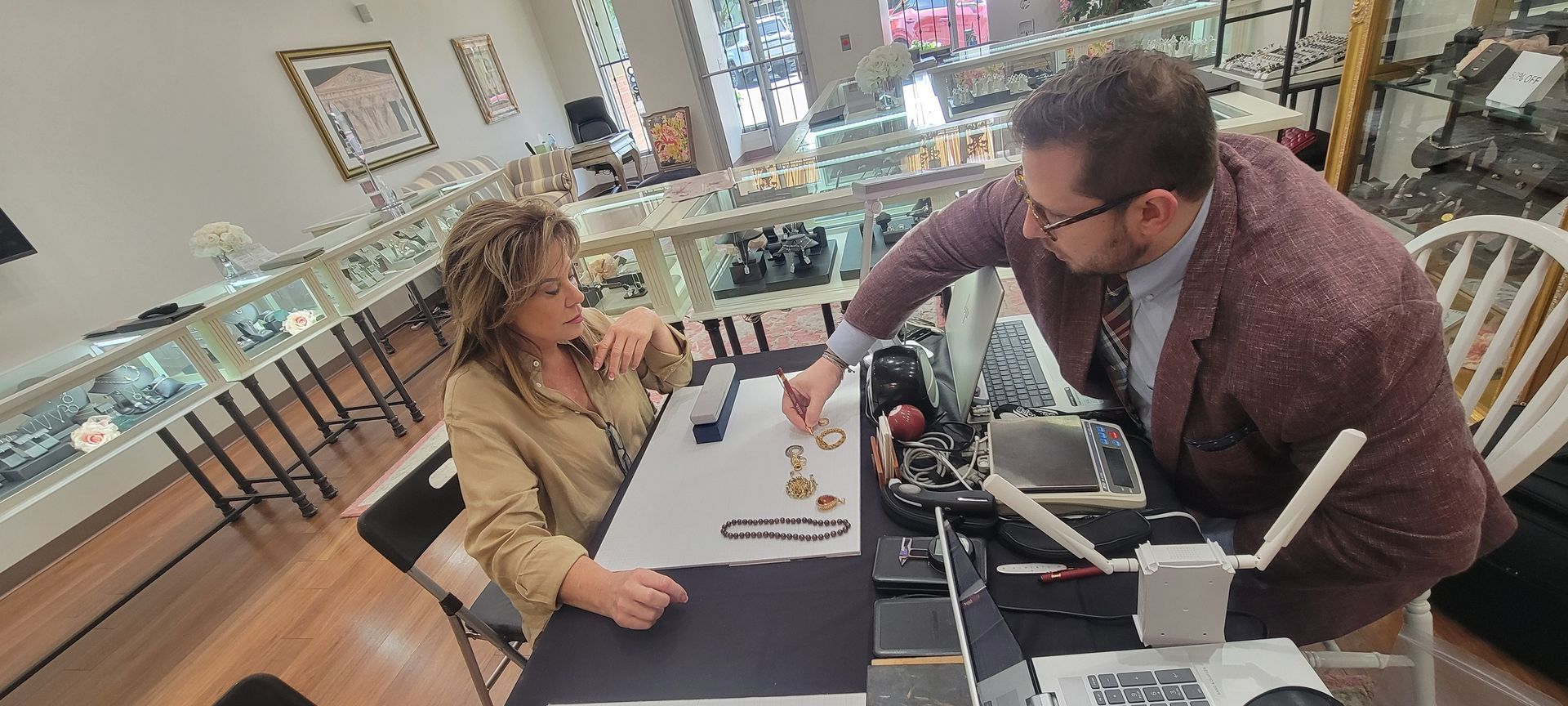 A woman and a man in a jewelry store examining jewelry at a counter. The man is pointing to the jewelry.