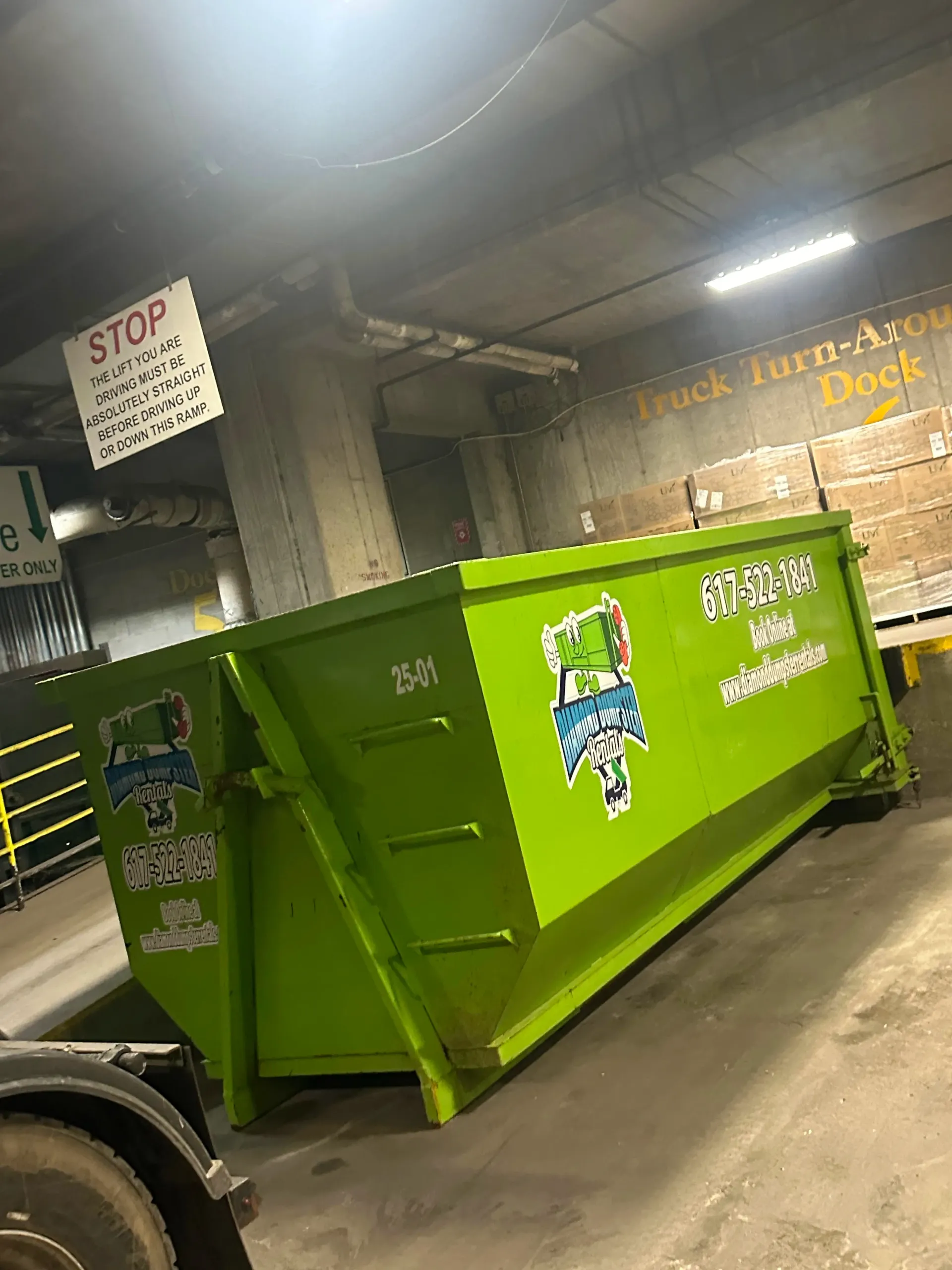 A green dumpster is sitting in a warehouse next to a truck.
