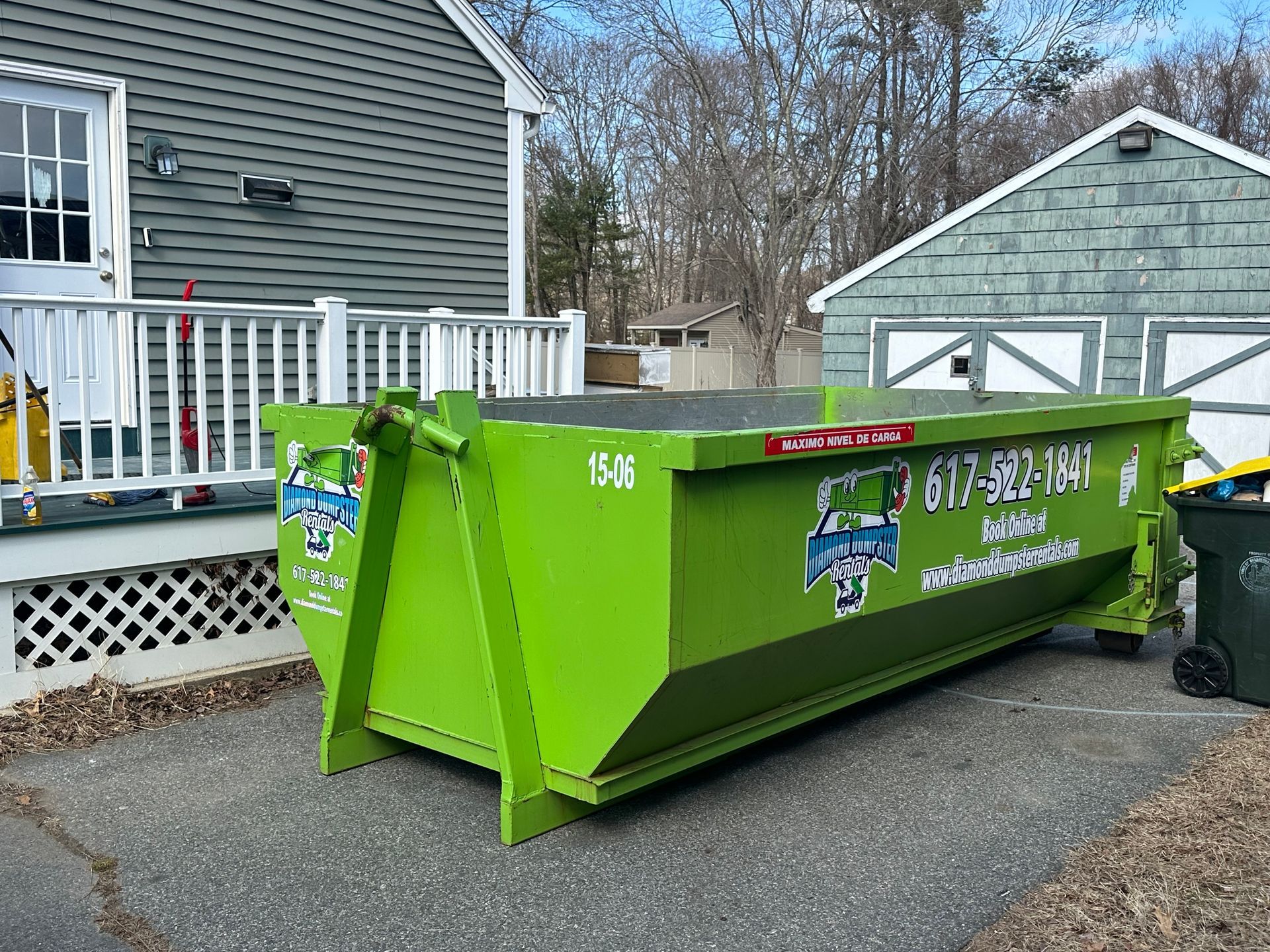 A green dumpster is parked in front of a house.