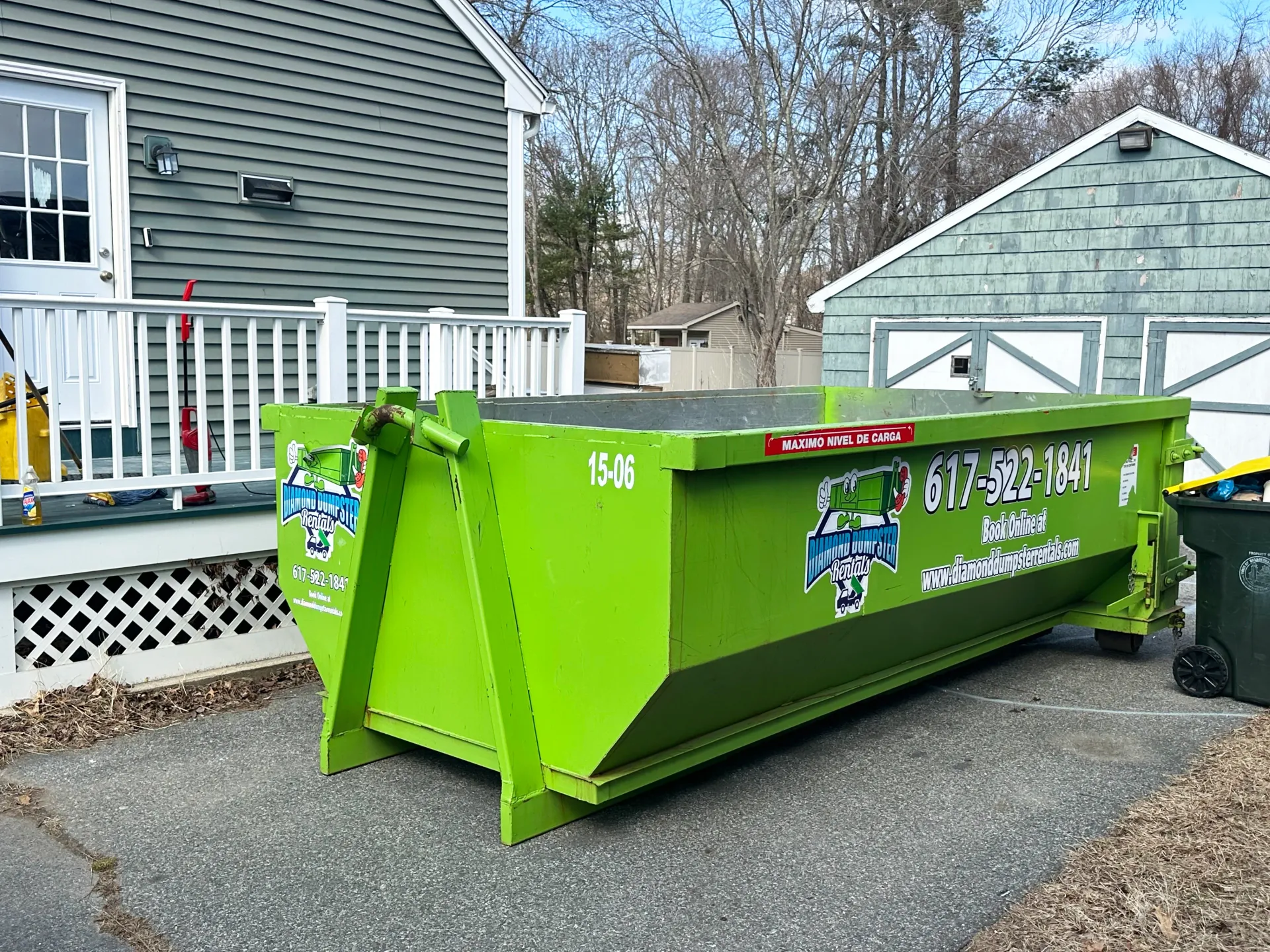 A green dumpster is parked in front of a house.