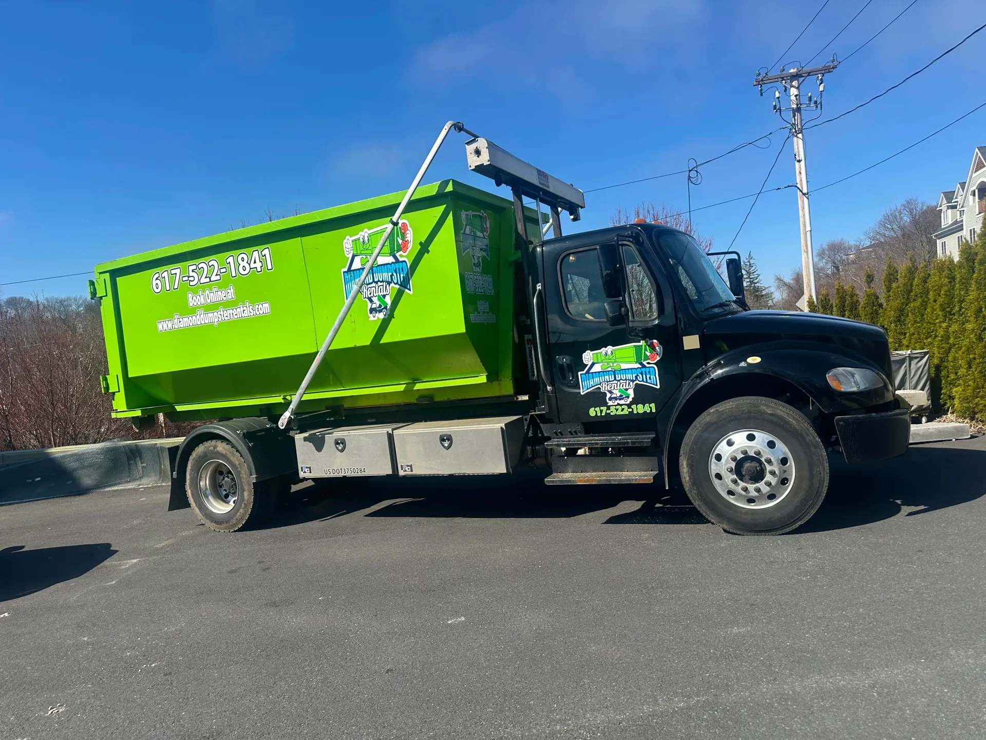 A green dumpster truck is parked on the side of the road.
