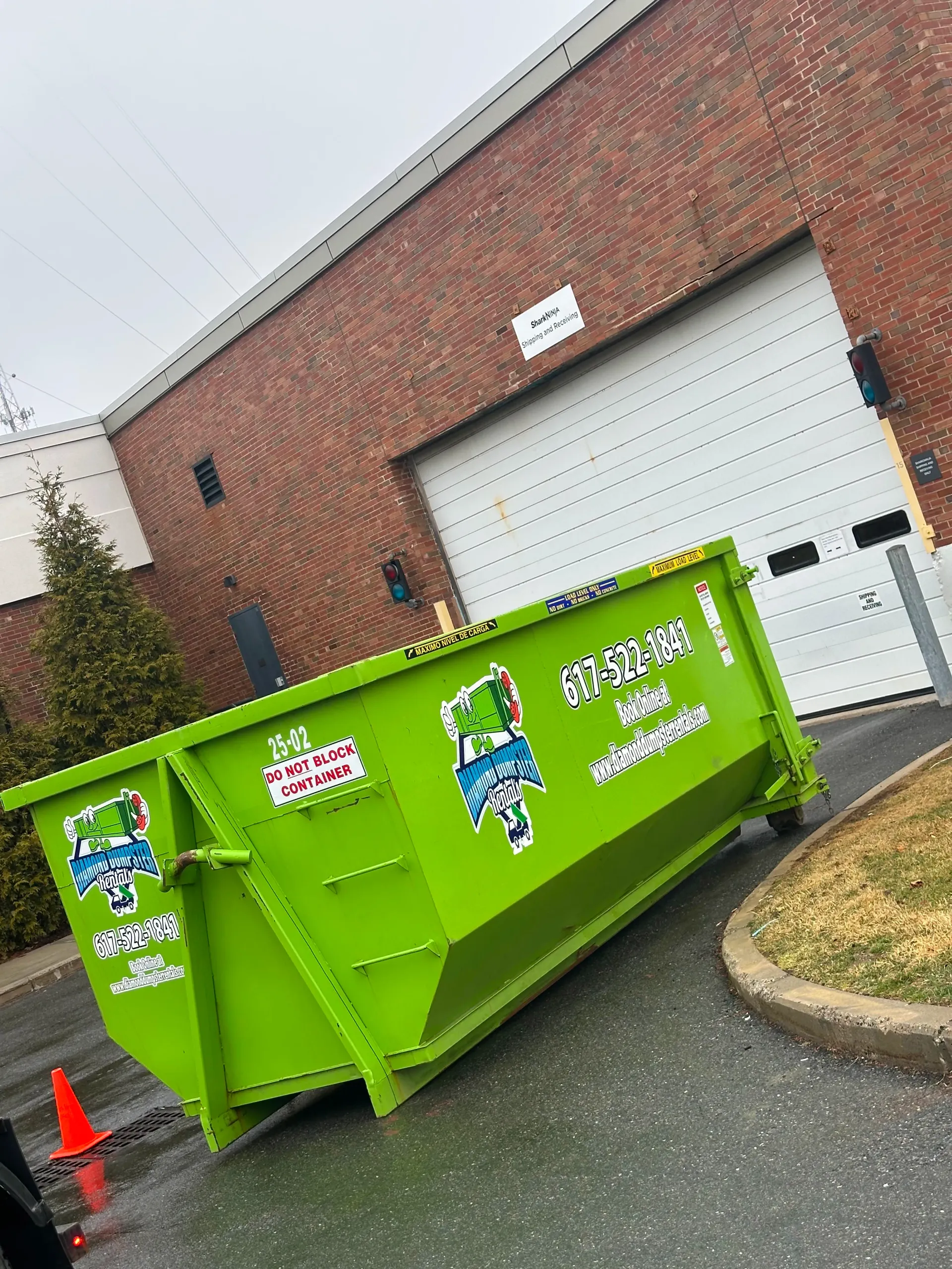 A green dumpster is parked in front of a brick building.
