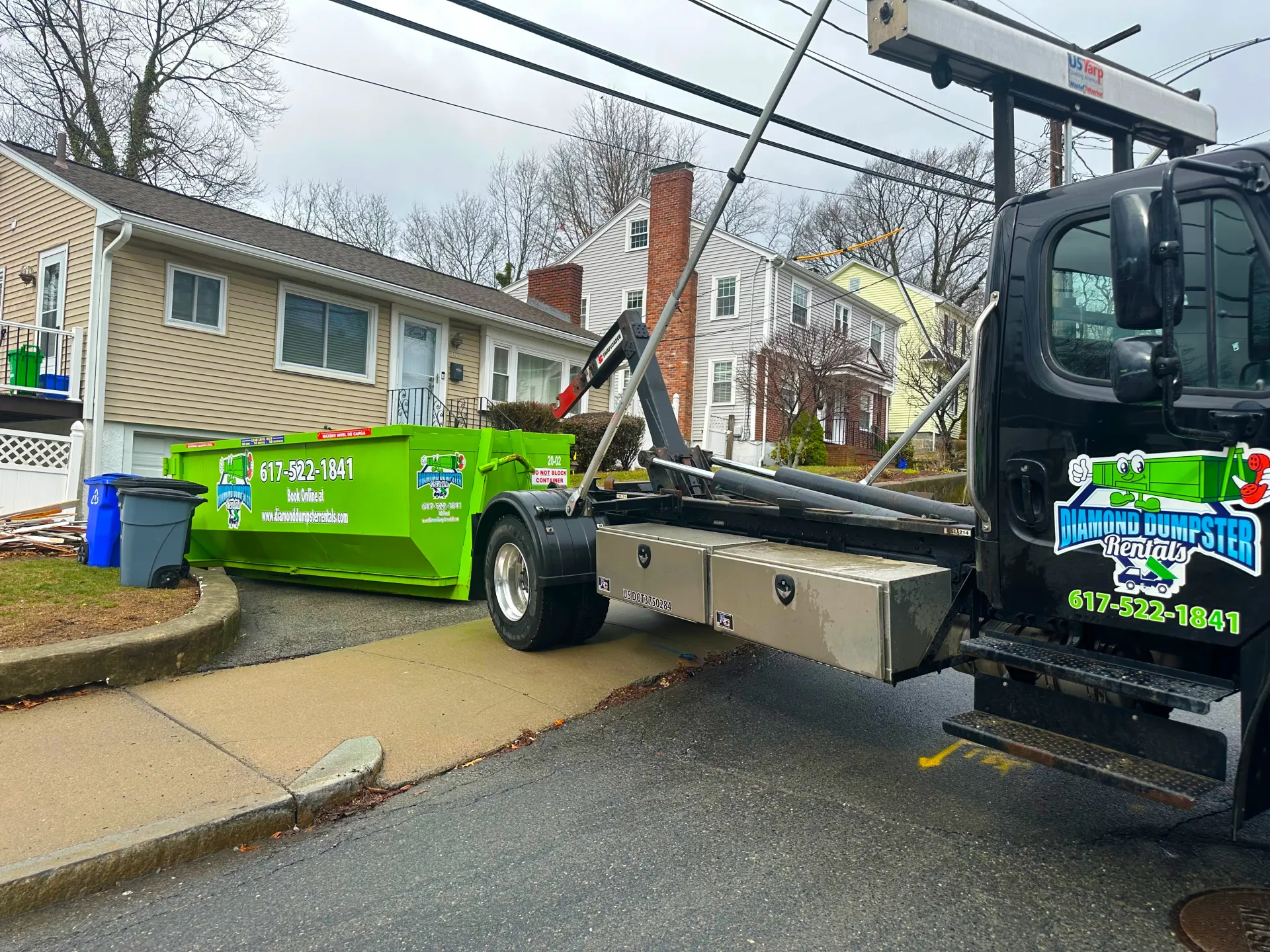 A dumpster is being towed by a tow truck in front of a house.