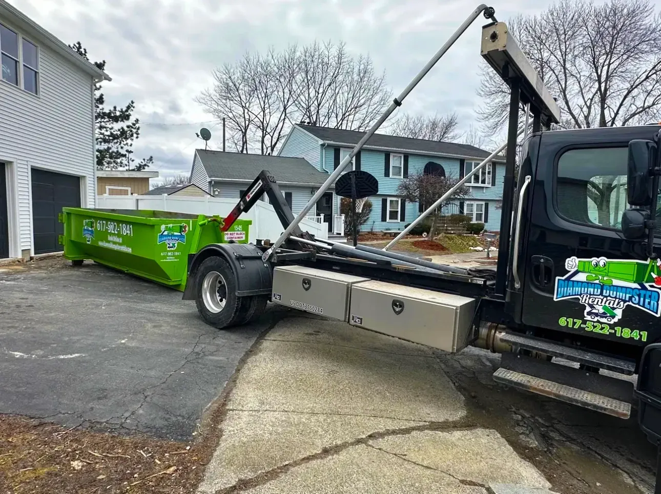 A dumpster is being towed by a dump truck in a driveway.