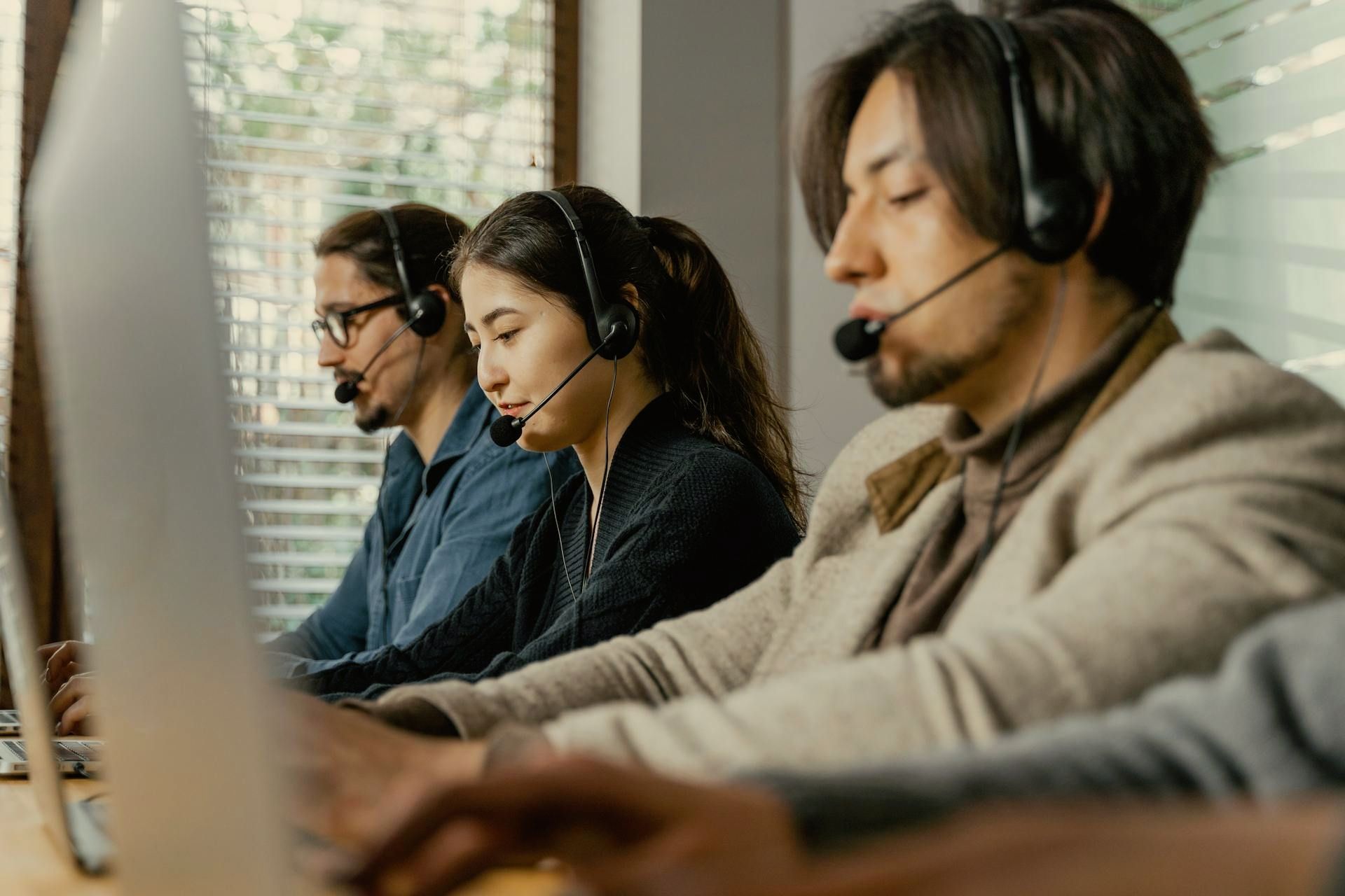 Three people wearing headsets working at computers in an office setting. Application support