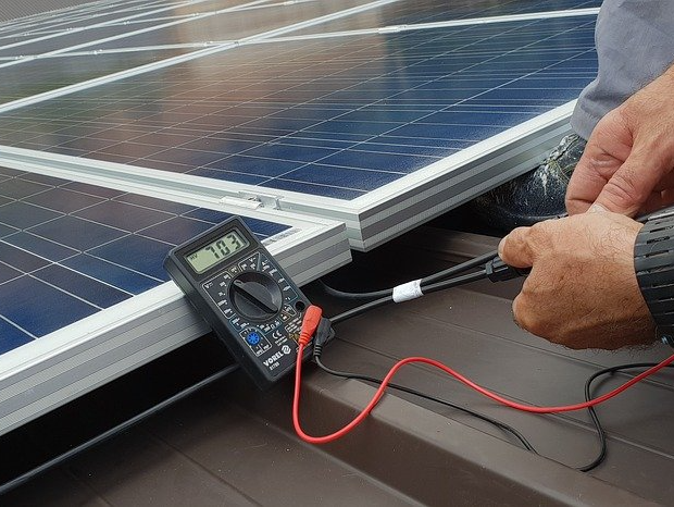 A person is working on a solar panel with a multimeter.