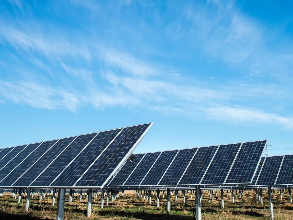 A row of solar panels in a field with a blue sky in the background.